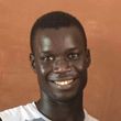 Un jeune homme en chemise blanche sourit à la caméra.