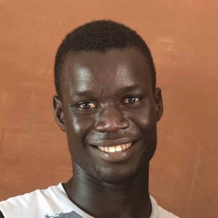 Un jeune homme en chemise blanche sourit à la caméra.