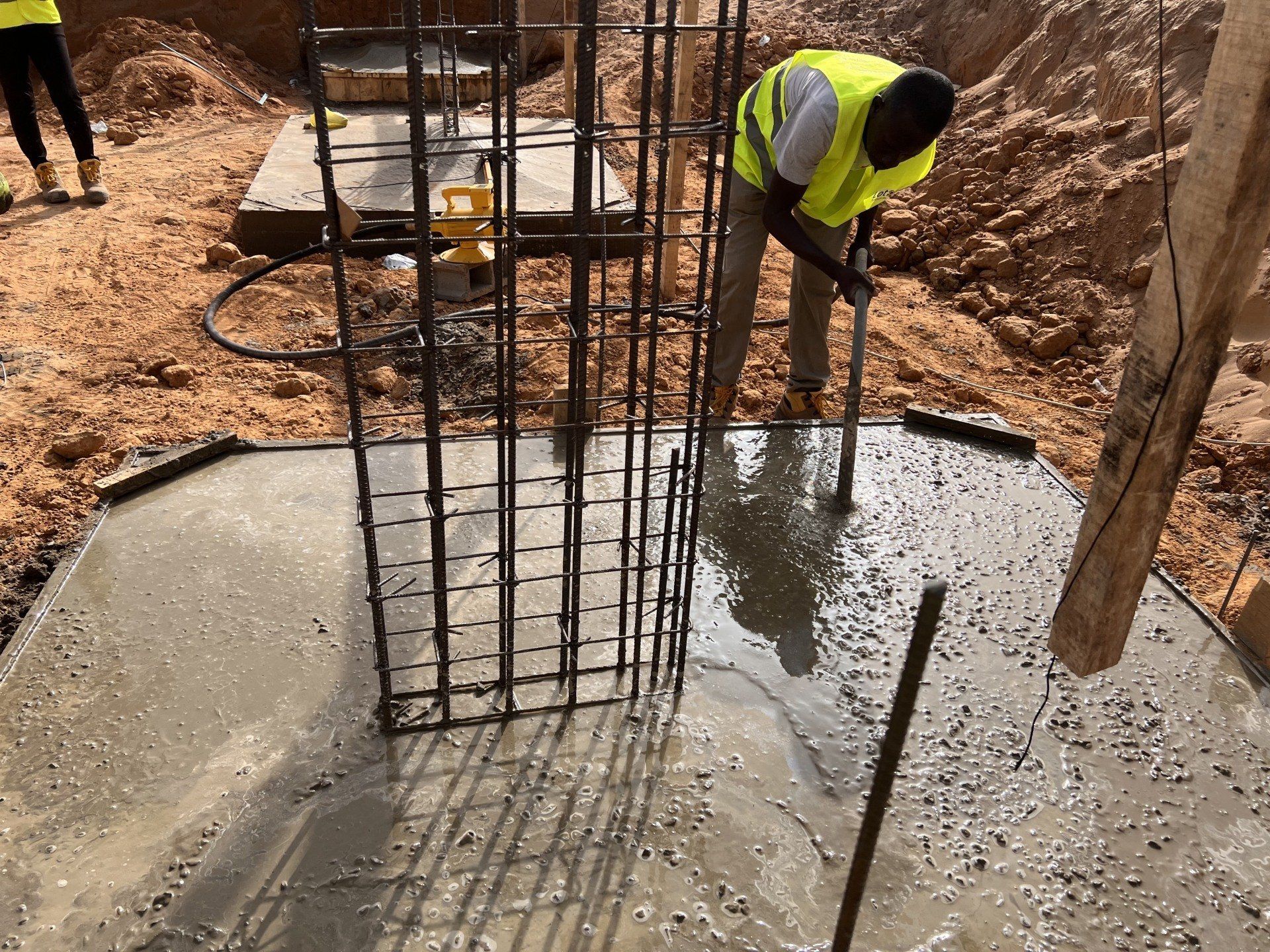 Un ouvrier du bâtiment verse du béton dans un trou dans le sol.