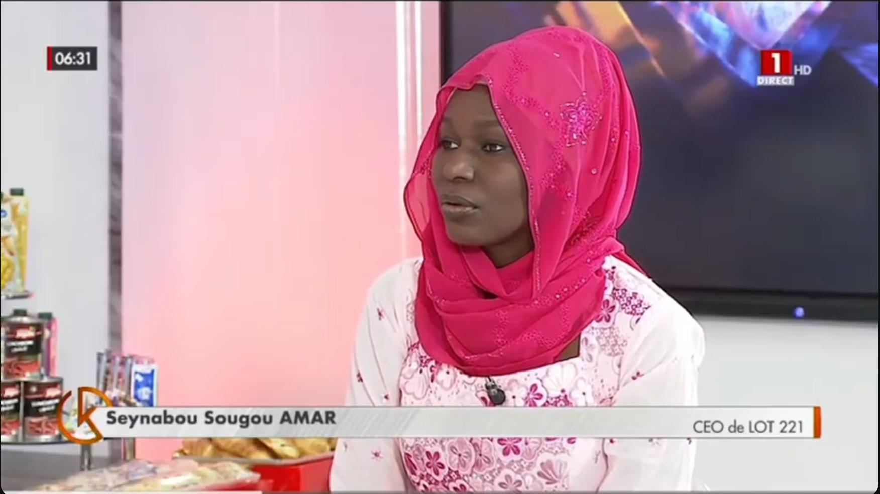 Une femme portant un hijab rose et une chemise blanche est interviewée dans une émission de télé