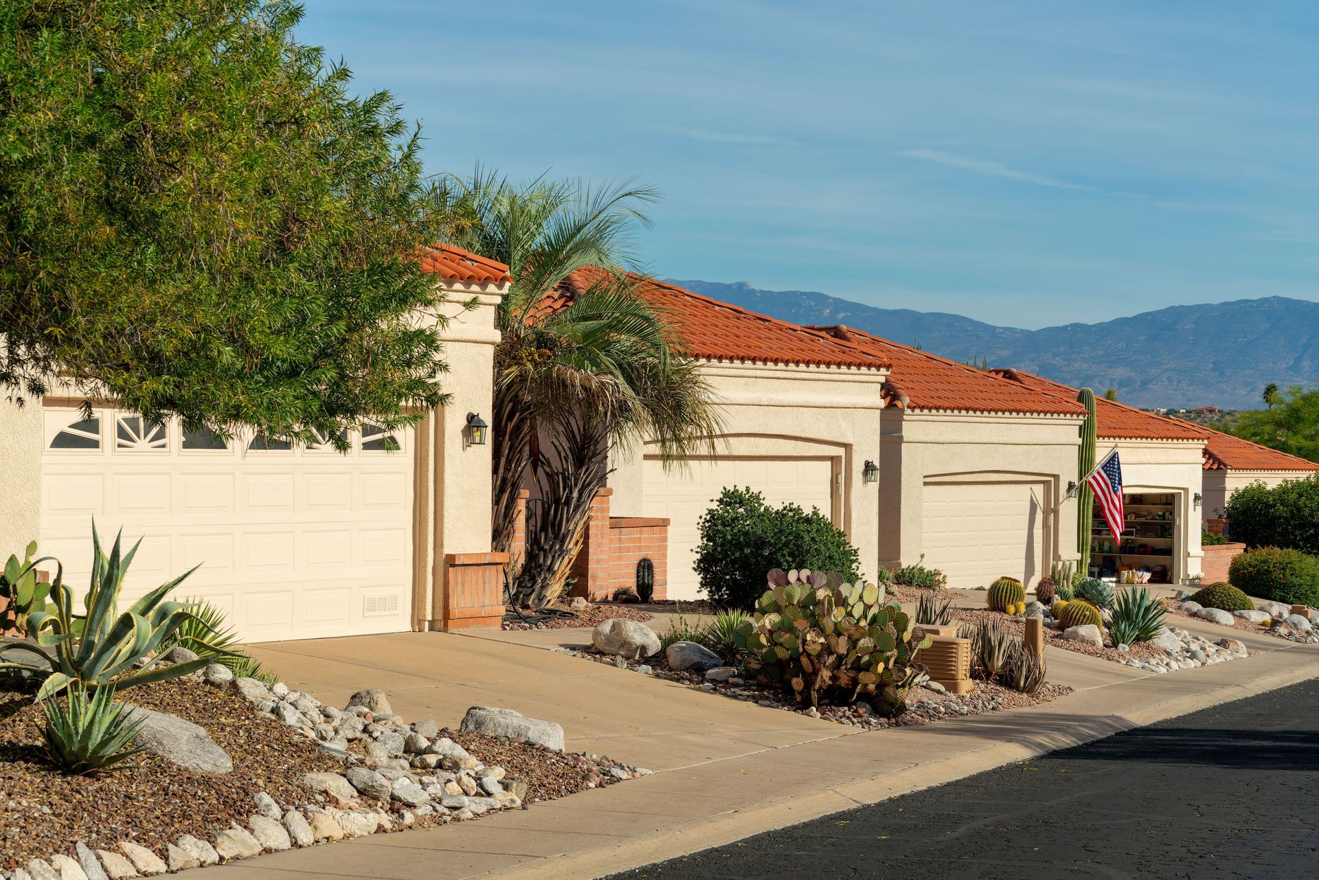 Row of beige houses with orange tile roofs and garage doors; desert landscaping.