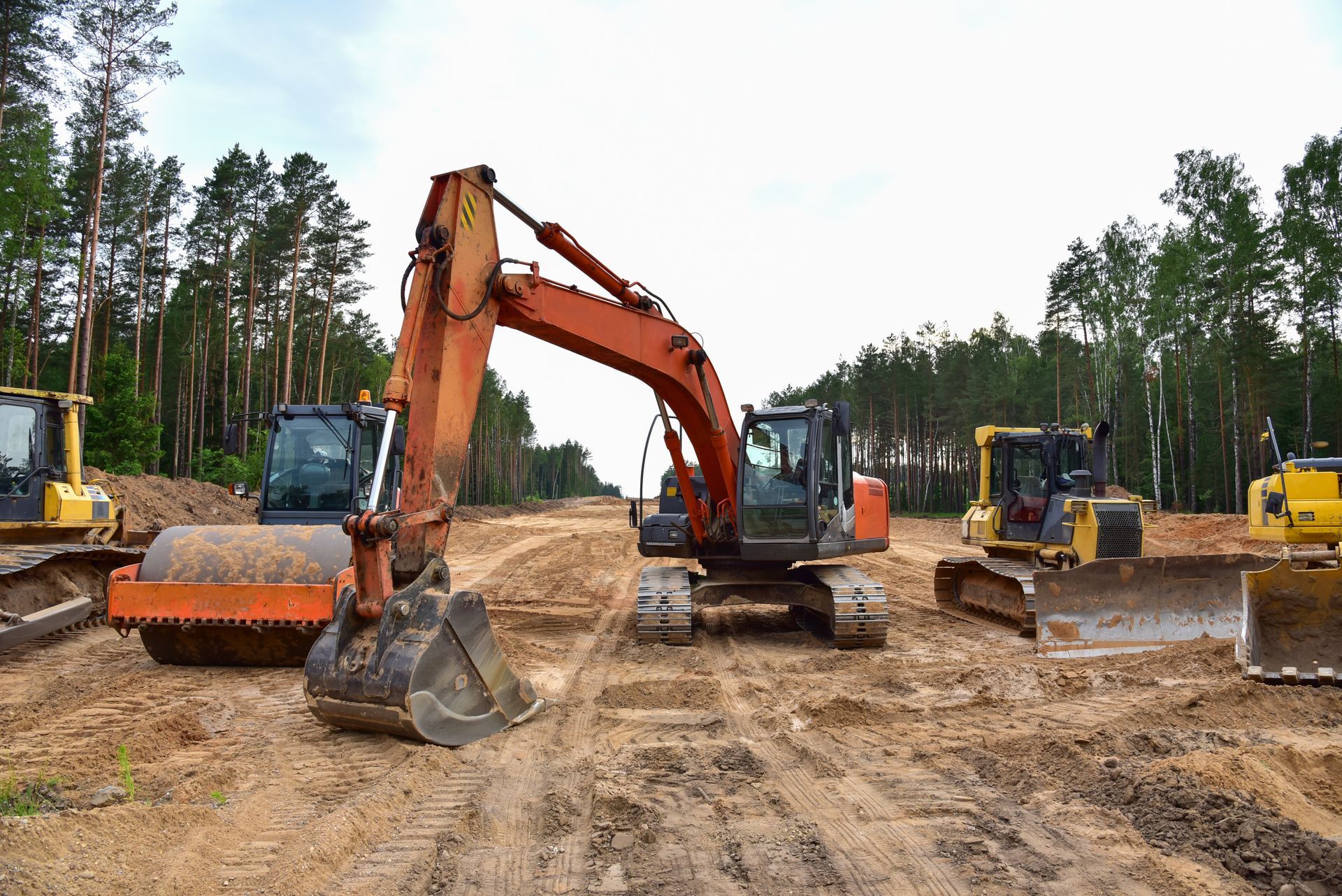 A group of construction vehicles are working on a dirt road.
