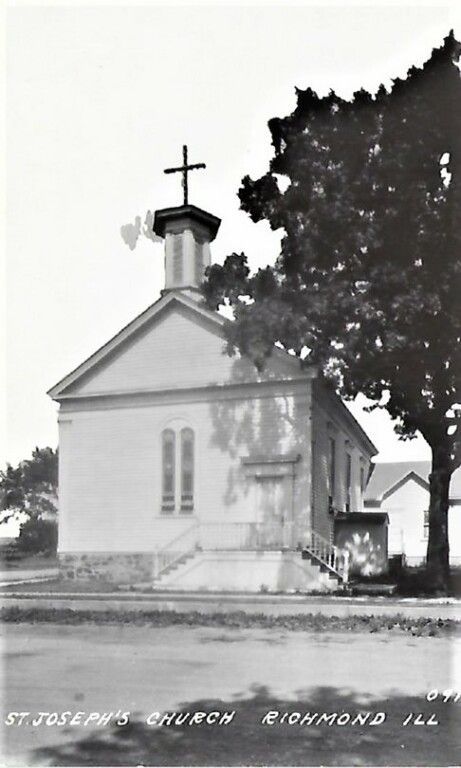 Small white church with a cross on the steeple beside a large tree, in black-and-white.