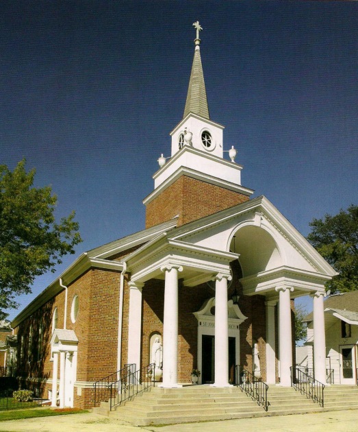 Brick church with white columns and tall steeple under a clear blue sky