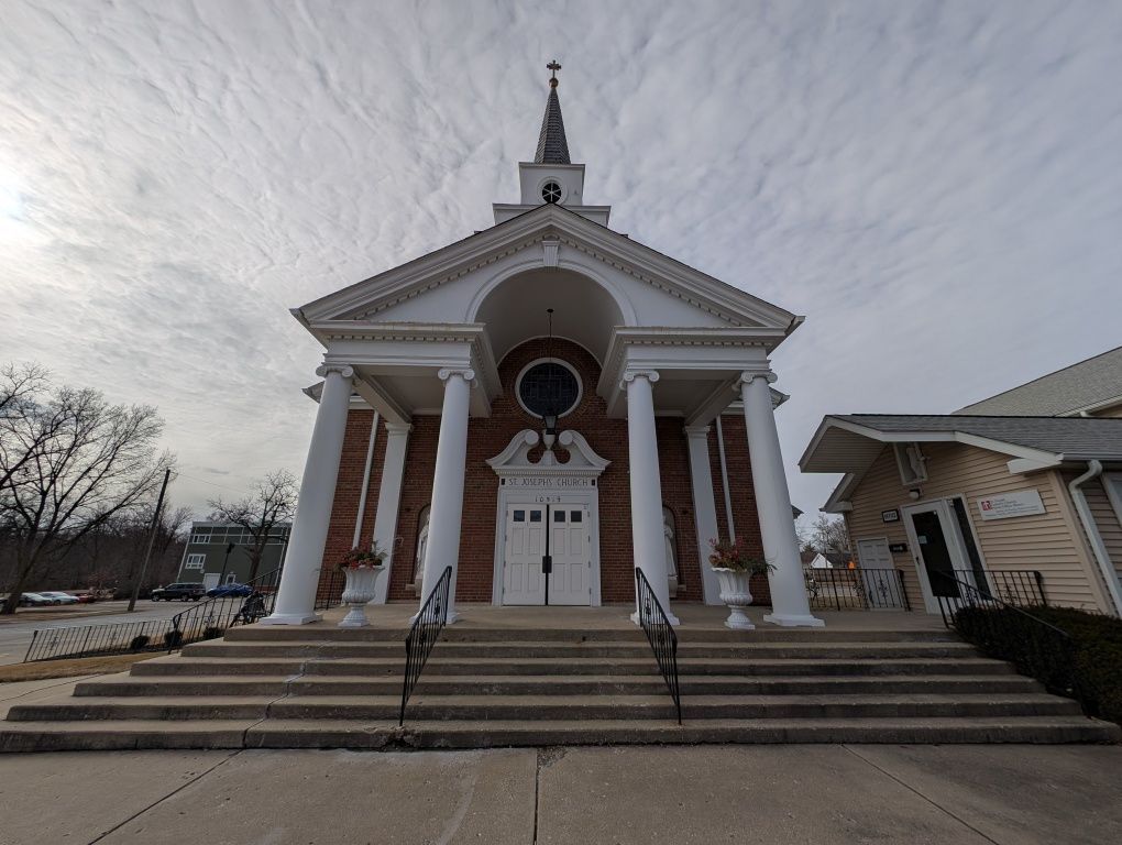 Brick church with white columns and steeple, viewed from the front under an overcast sky