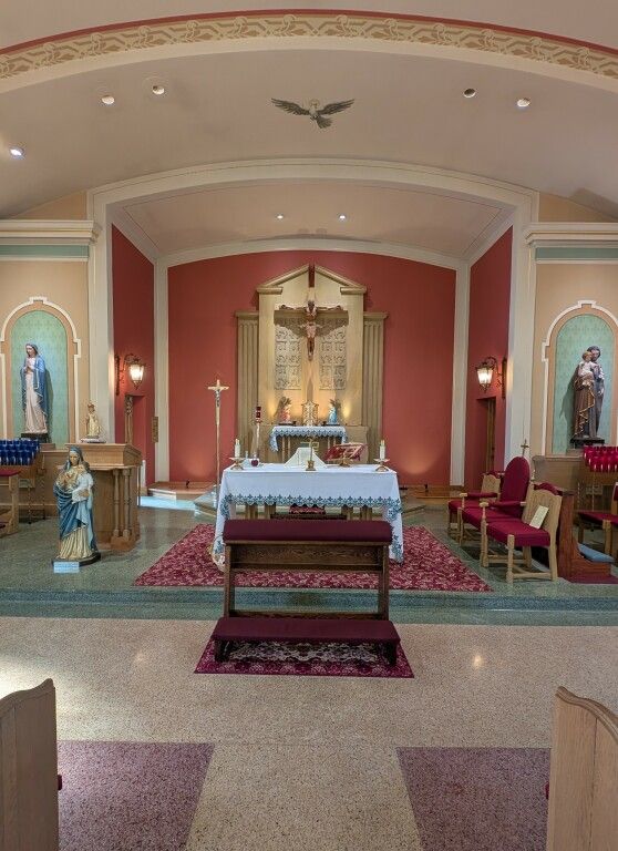 Church altar with white cloth, red walls, candles, and religious statues in side alcoves.