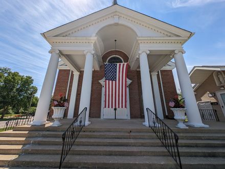 Brick building entrance with white columns and an American flag hanging over the front steps