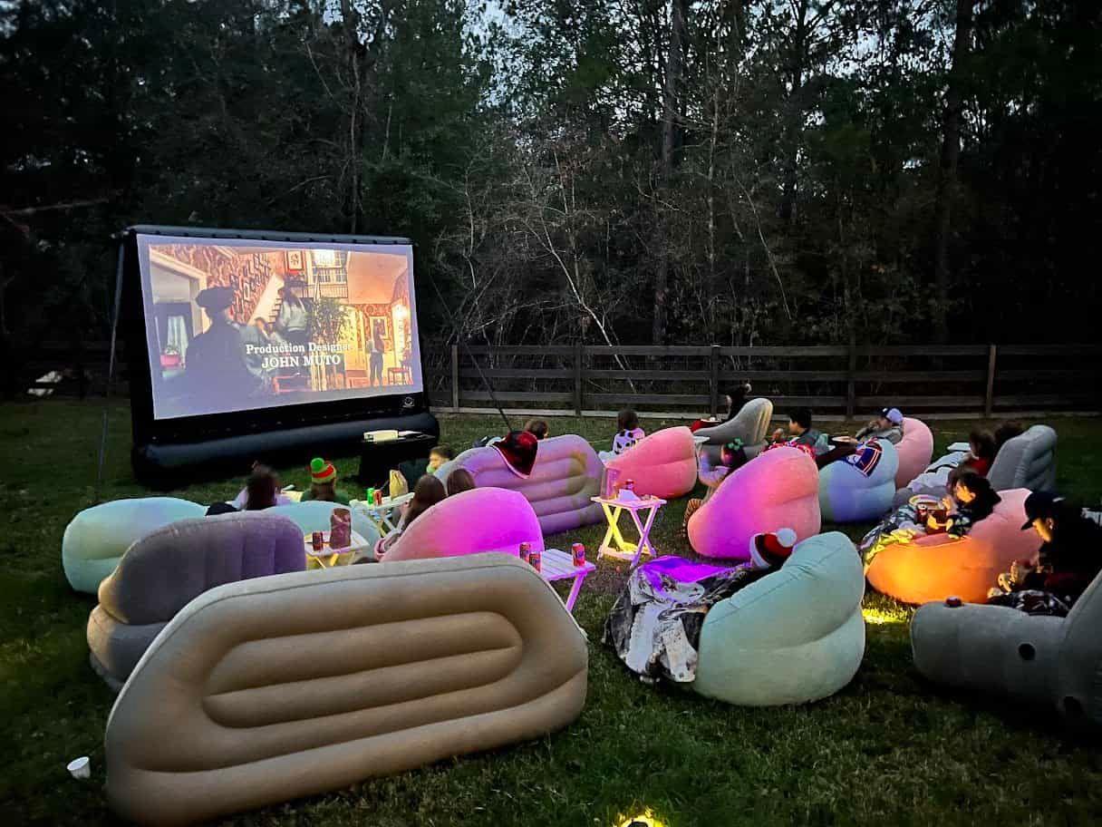 A group of people are sitting in the grass watching a movie on an inflatable screen.