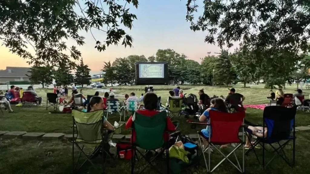 A large group of people are sitting in chairs in front of a large screen.