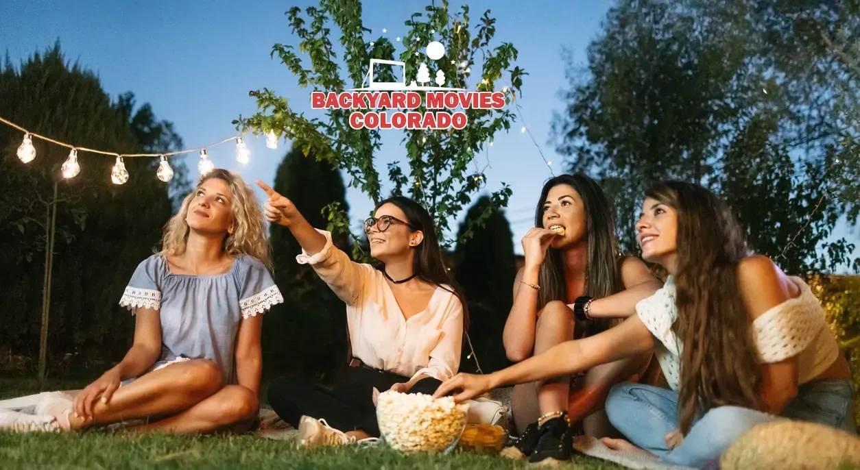 Four women watching an outdoor movie and eating popcorn