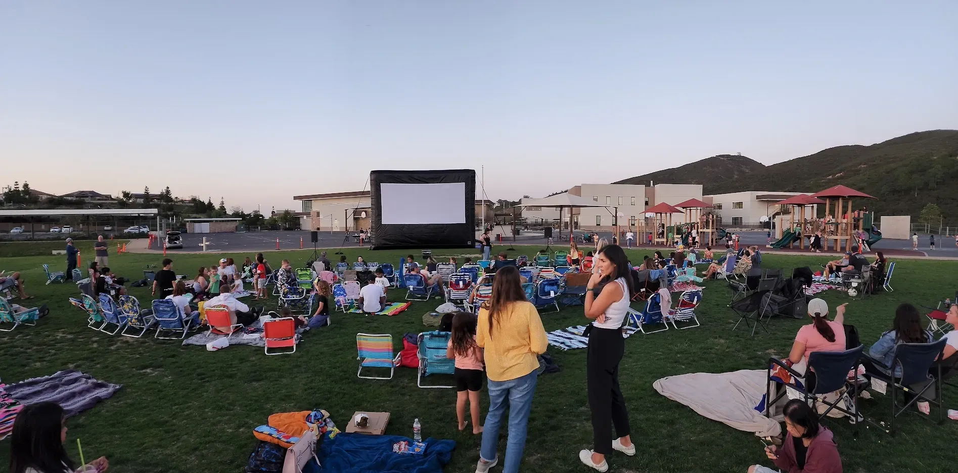 A large group of people are sitting in a field watching a movie