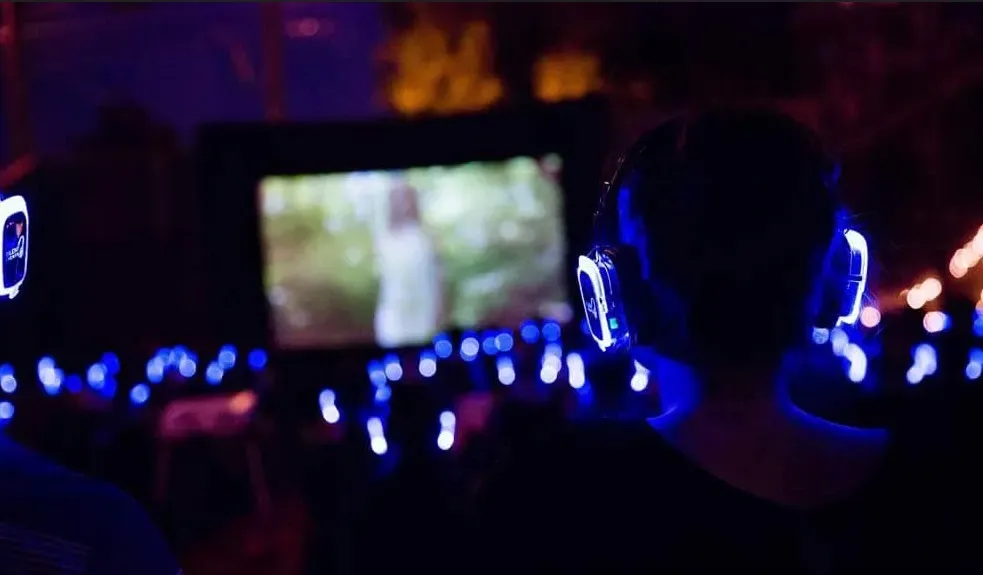 A group of people wearing headphones  watching a movie outside under the stars