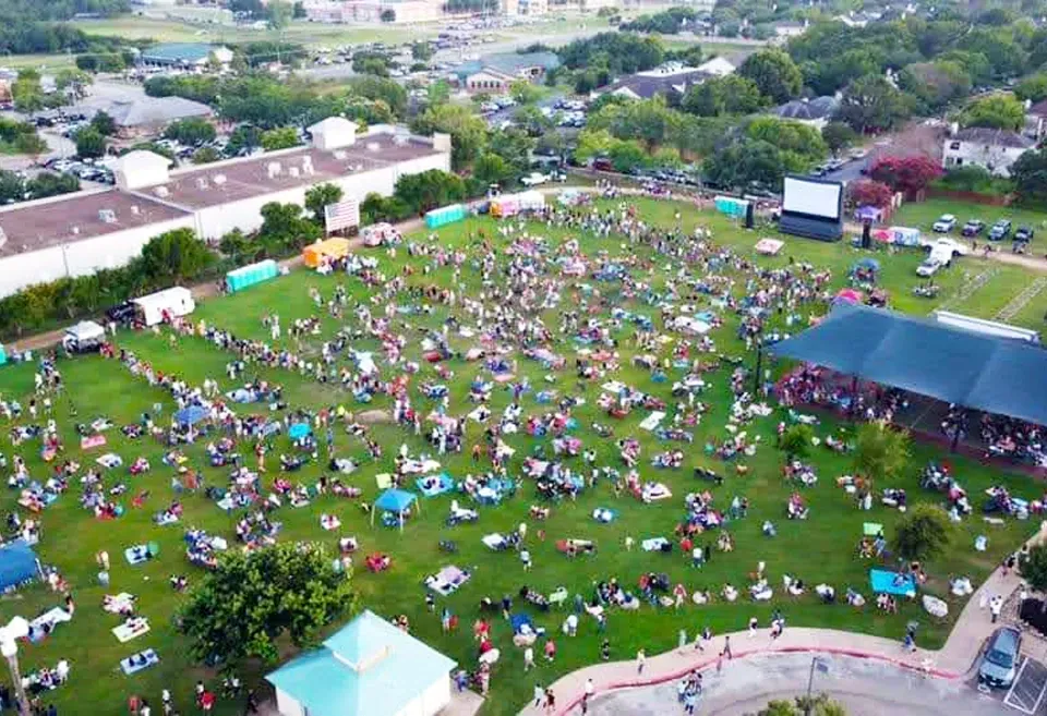 A group of people are watching a movie on a large screen in a park