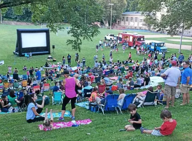A large group of people are sitting in the grass watching a movie.