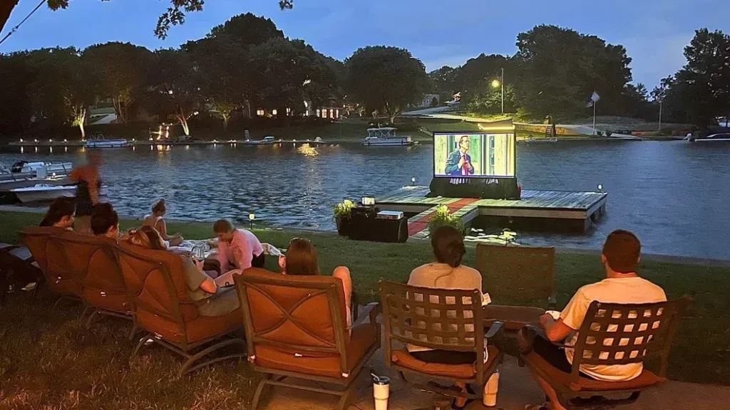 A group of people are sitting outside watching a movie on a projector screen