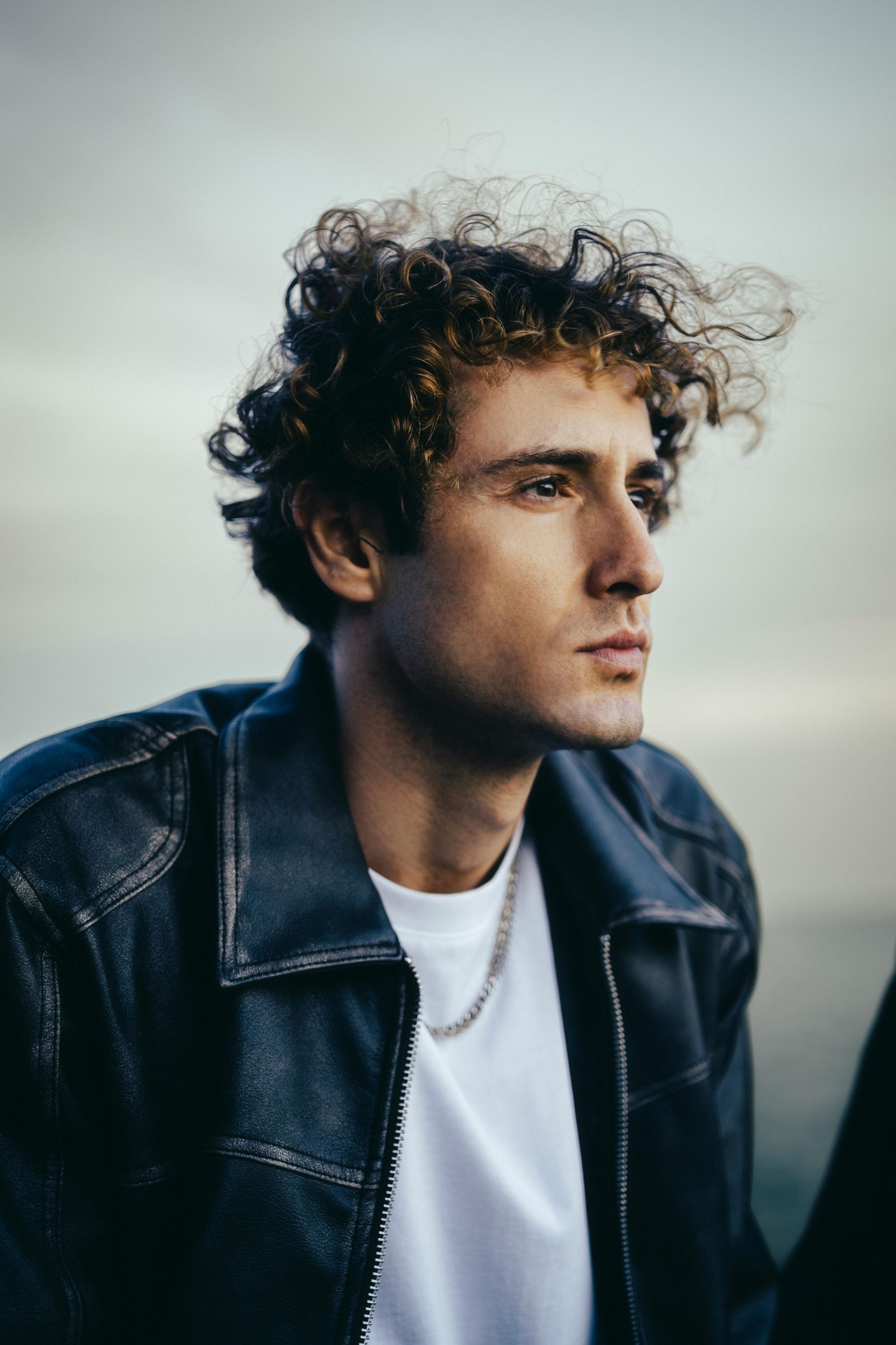 A young man with curly hair is wearing a black leather jacket and a white shirt.