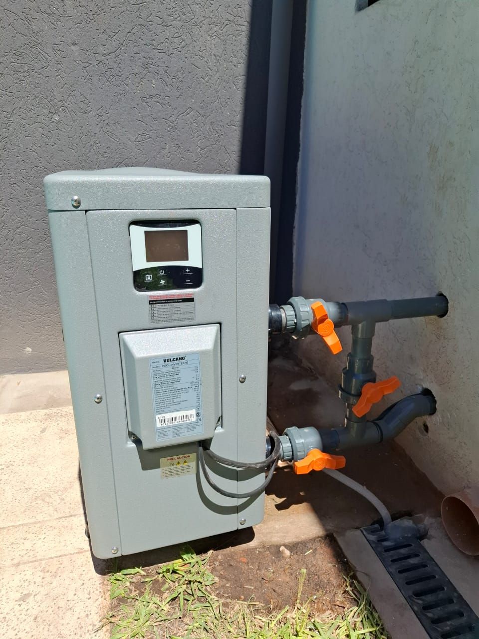 Un calentador de piscina está ubicado en el costado de un edificio, al lado de un desagüe.