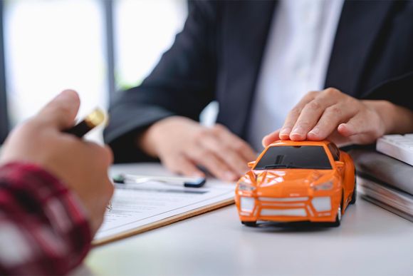 a person holding an orange toy car in front of a clipboard