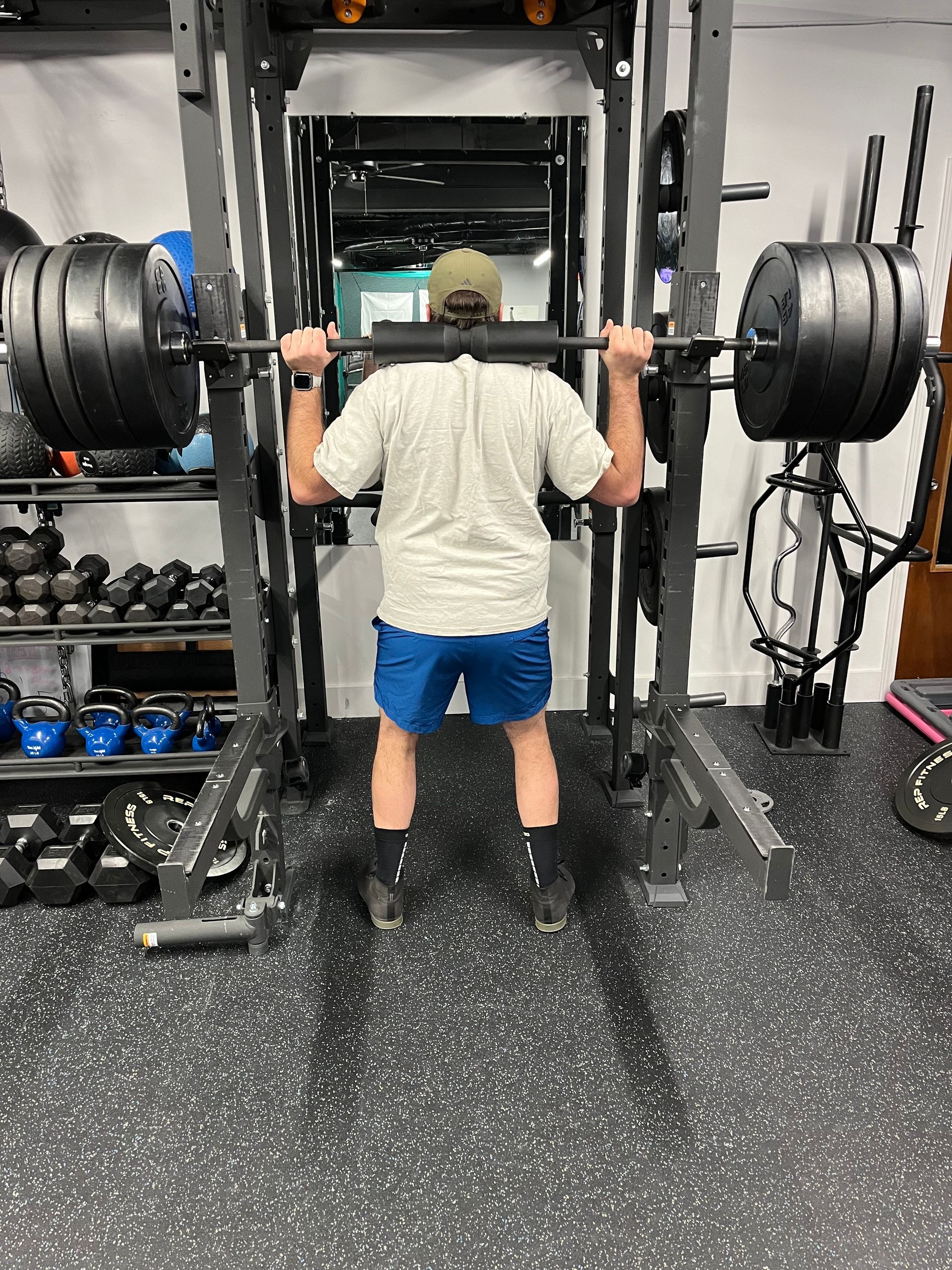 A man is squatting with a barbell over his head in a gym.