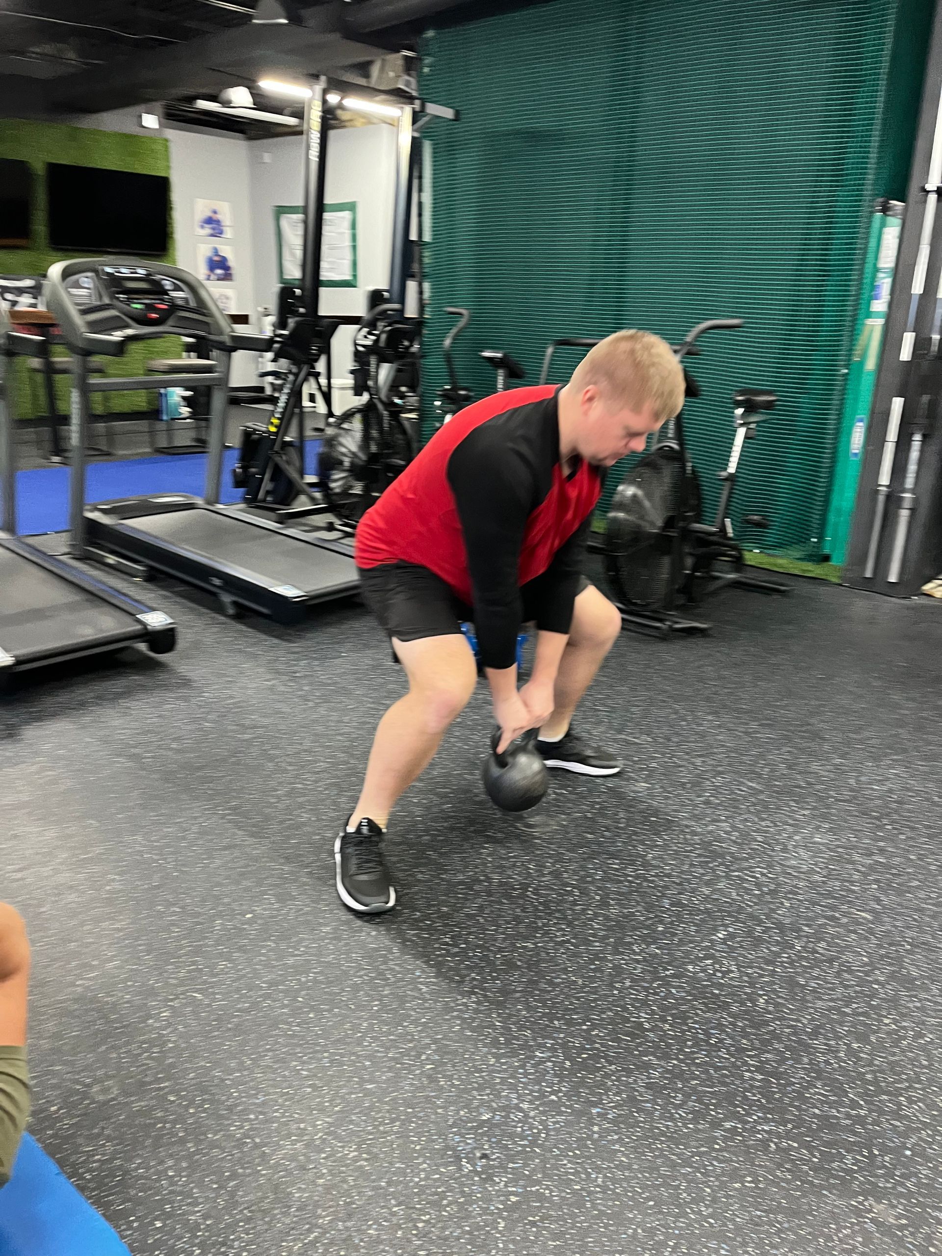 A man is squatting down with a kettlebell in a gym.