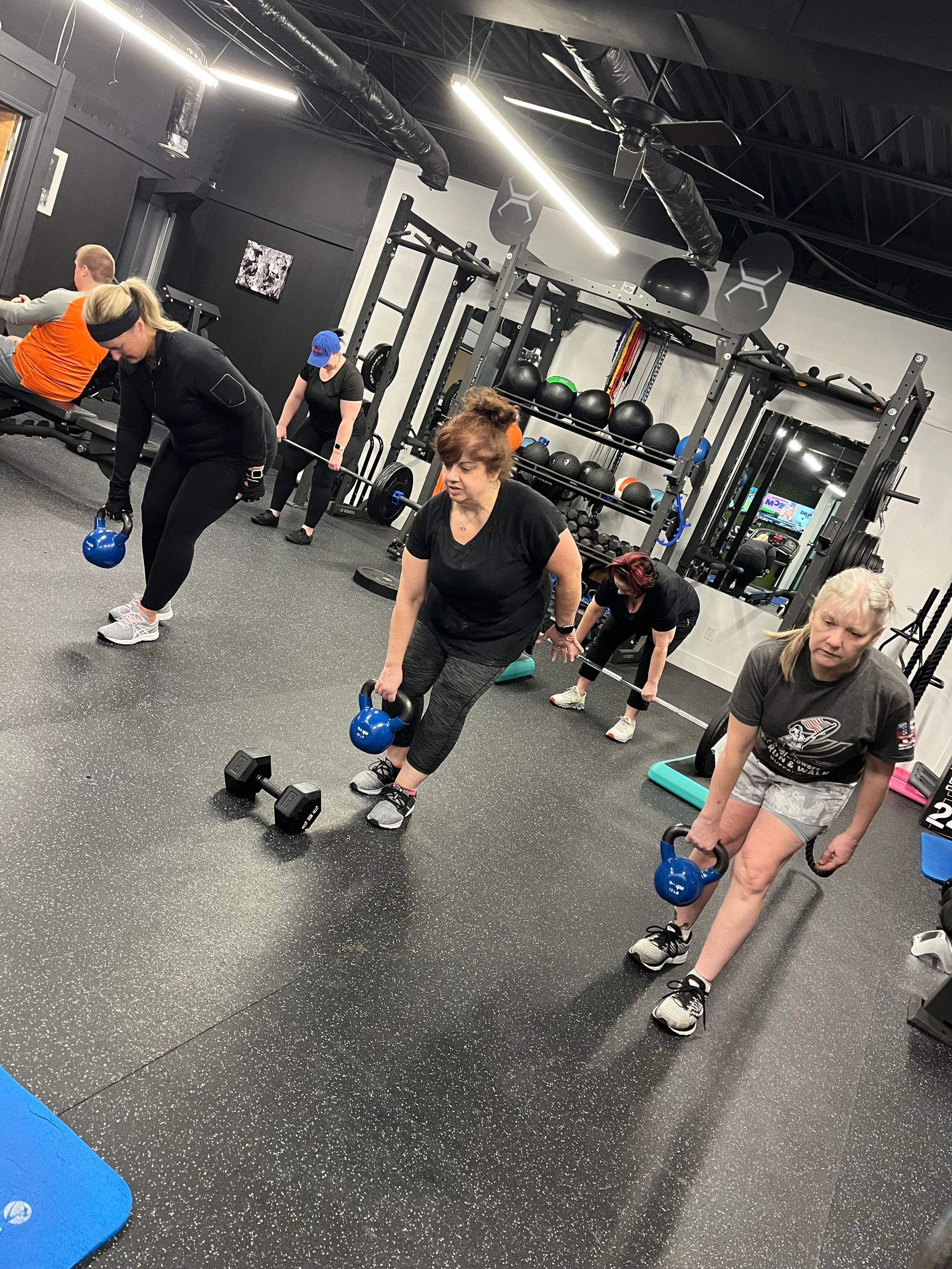 A group of people are doing exercises with kettlebells in a gym.