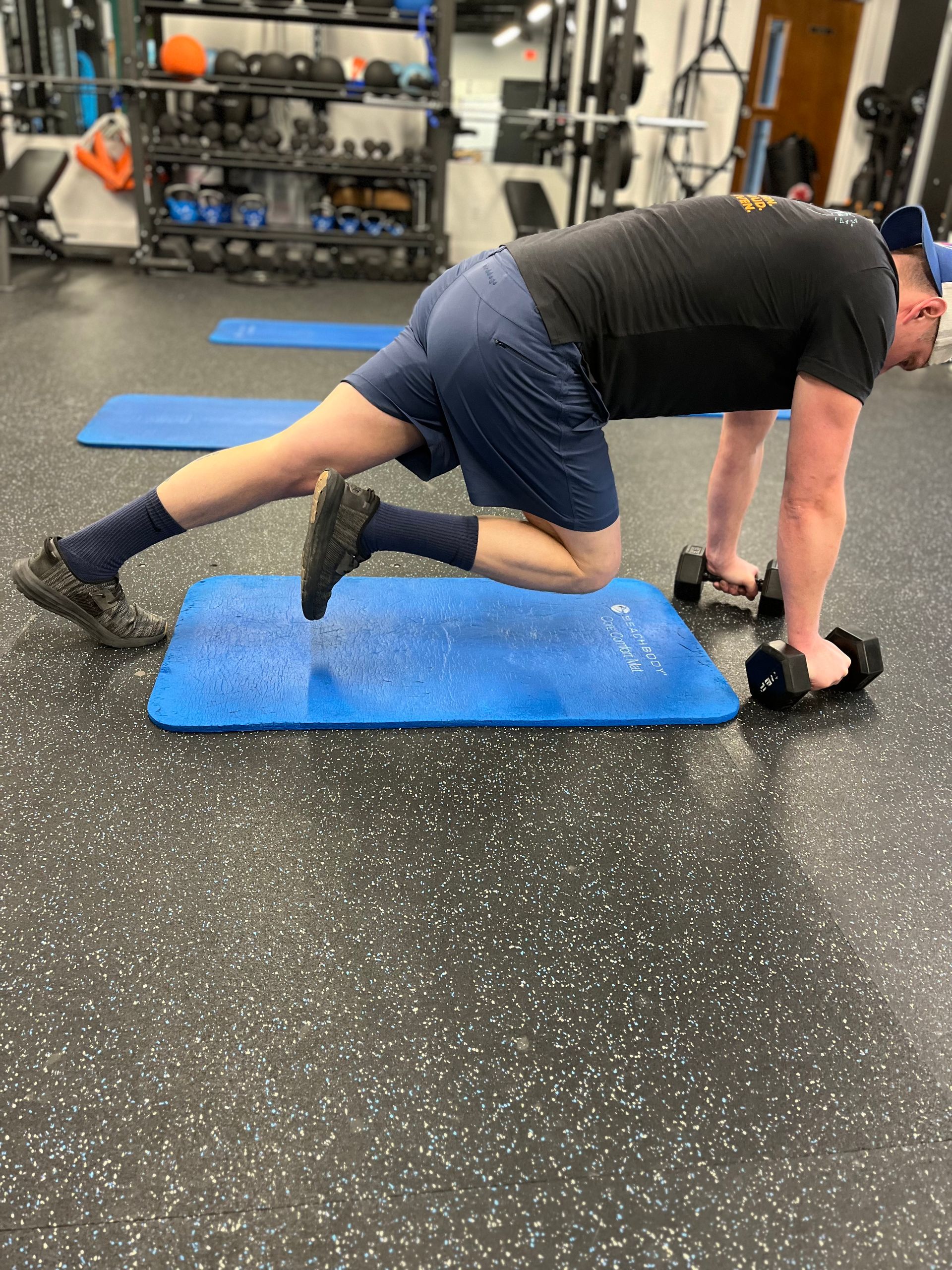 A man is doing push ups on a blue mat in a gym.