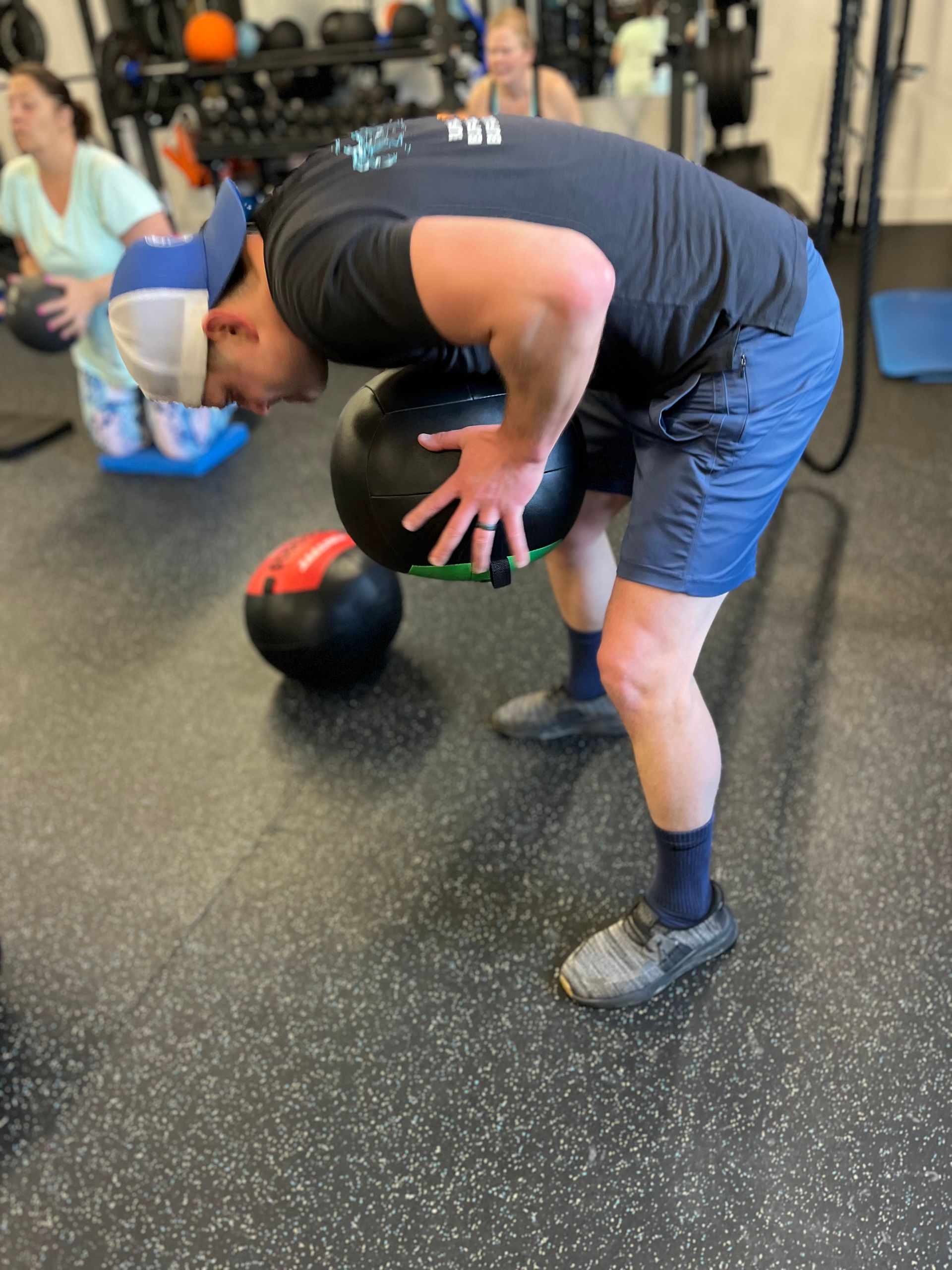 A man is bending over to pick up a medicine ball in a gym.