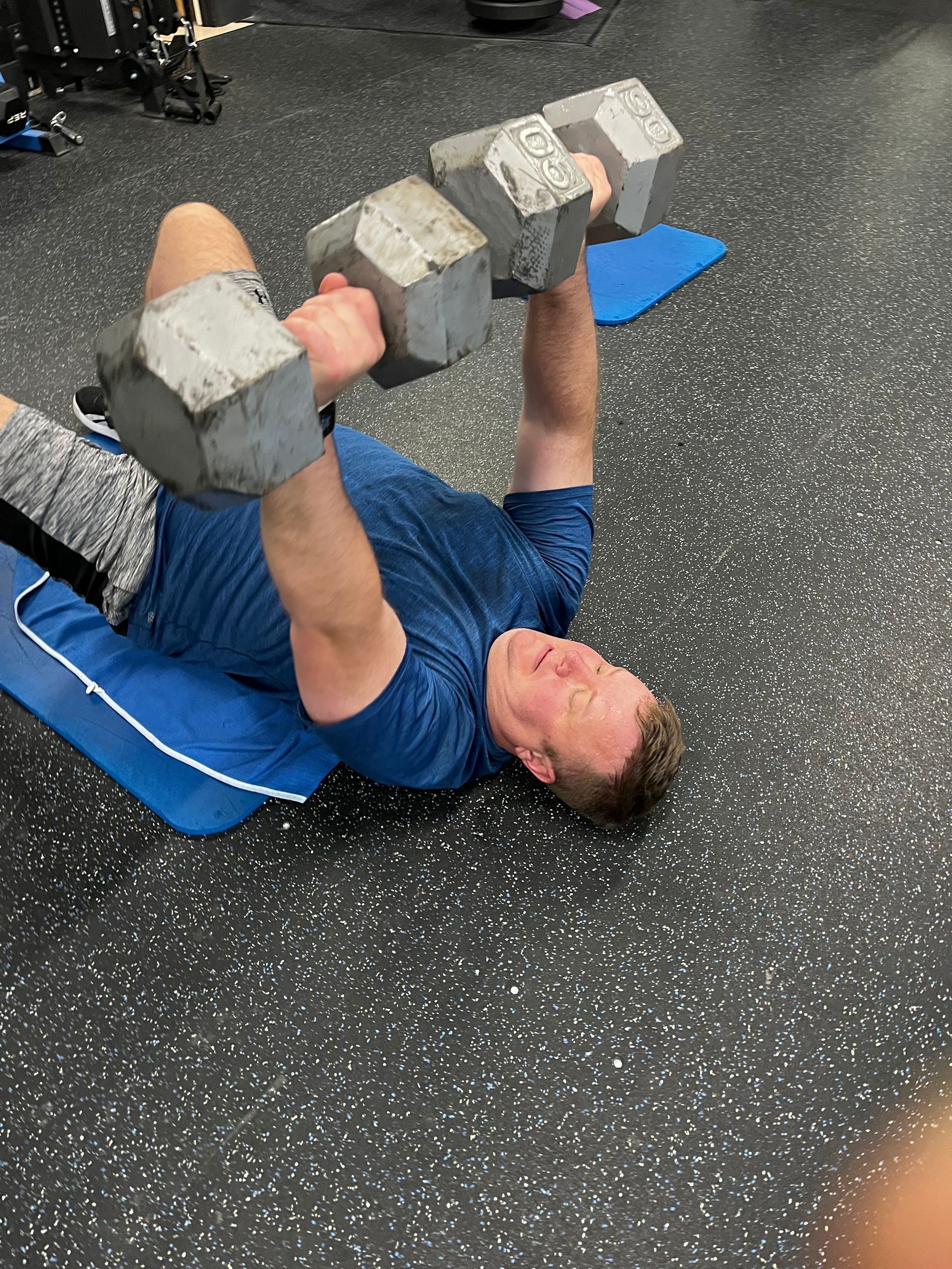 A man is laying on the floor lifting dumbbells.