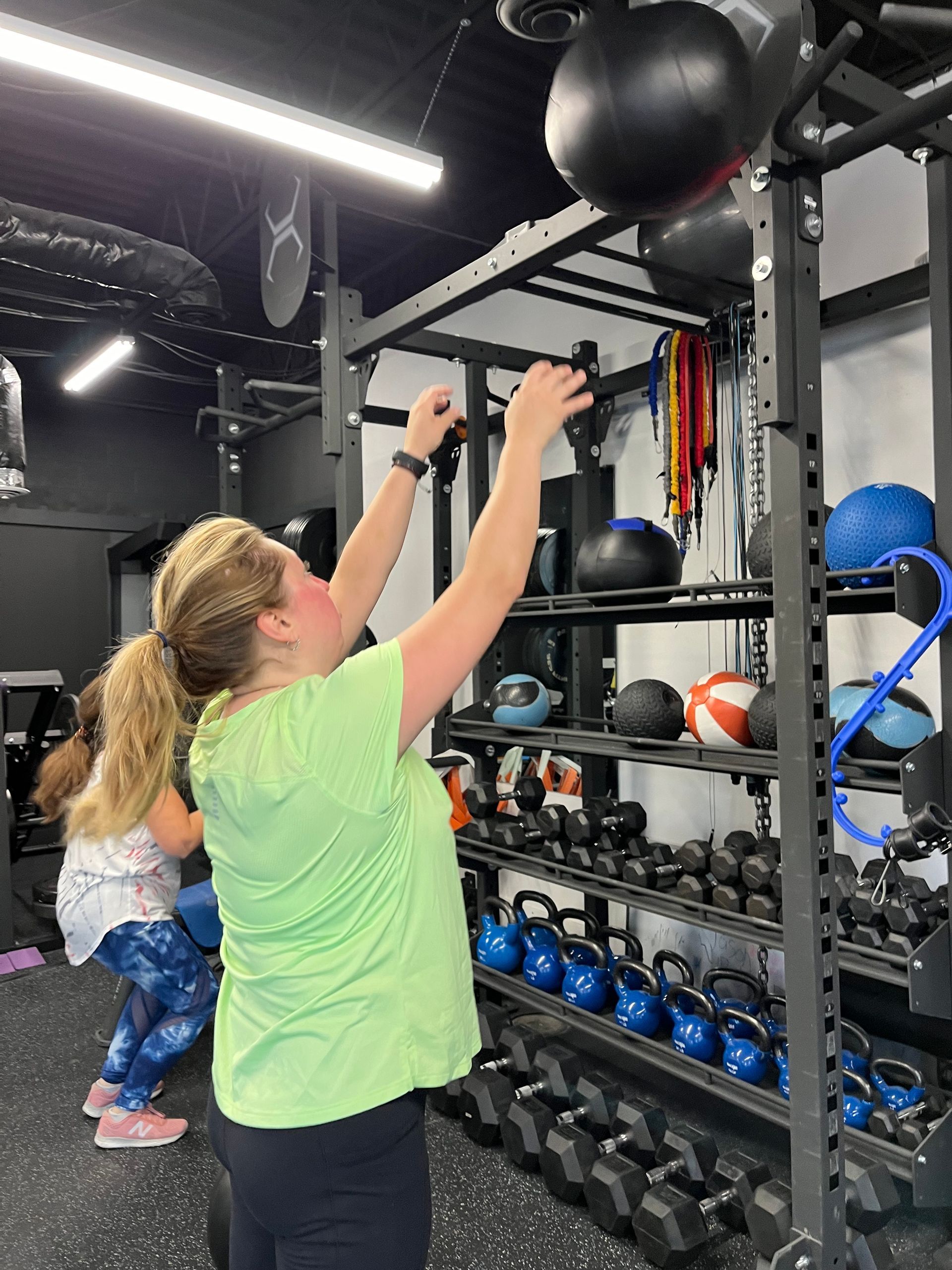A woman is reaching for a ball in a gym.