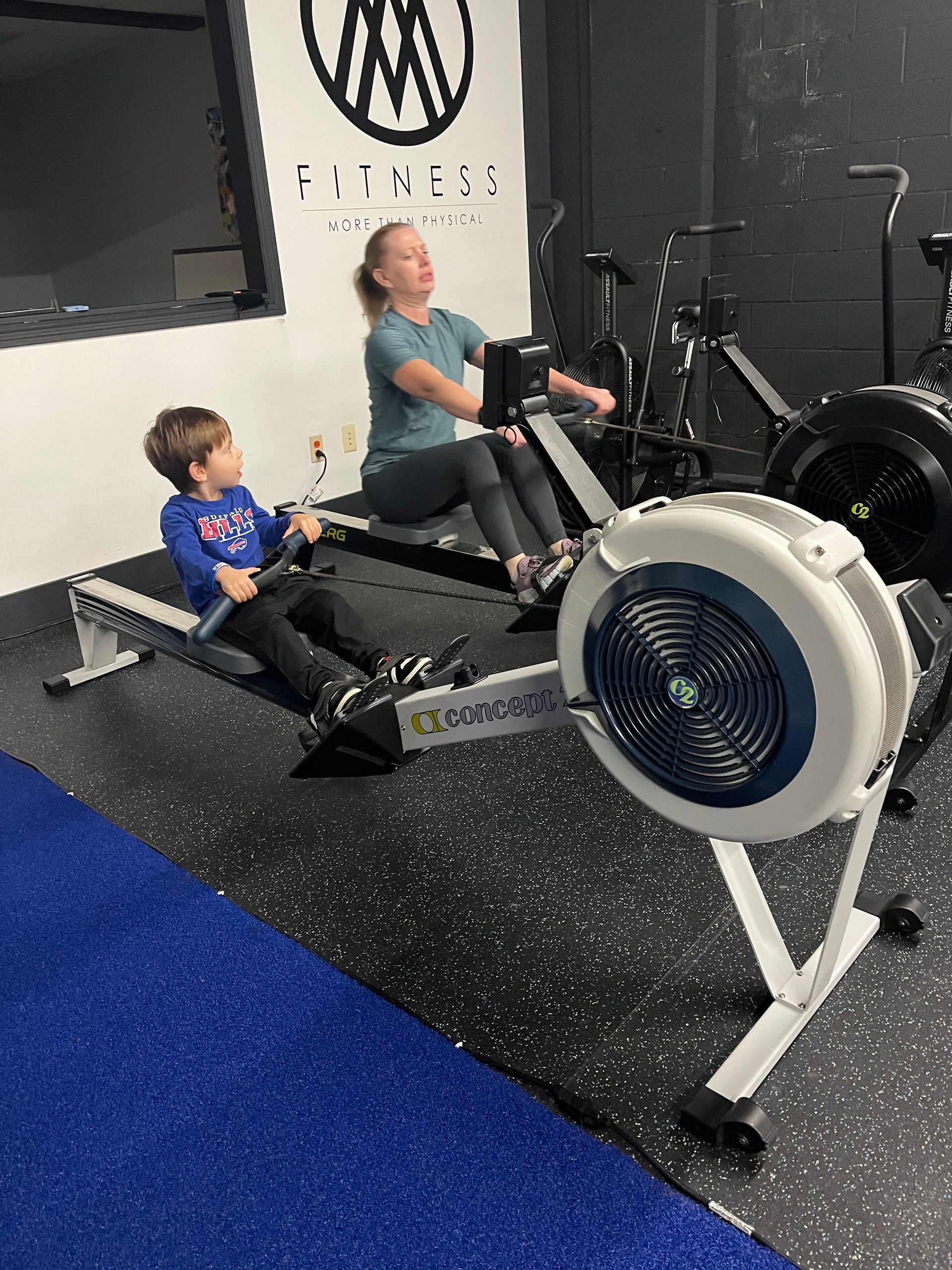 A woman and a child are riding rowing machines in a gym.
