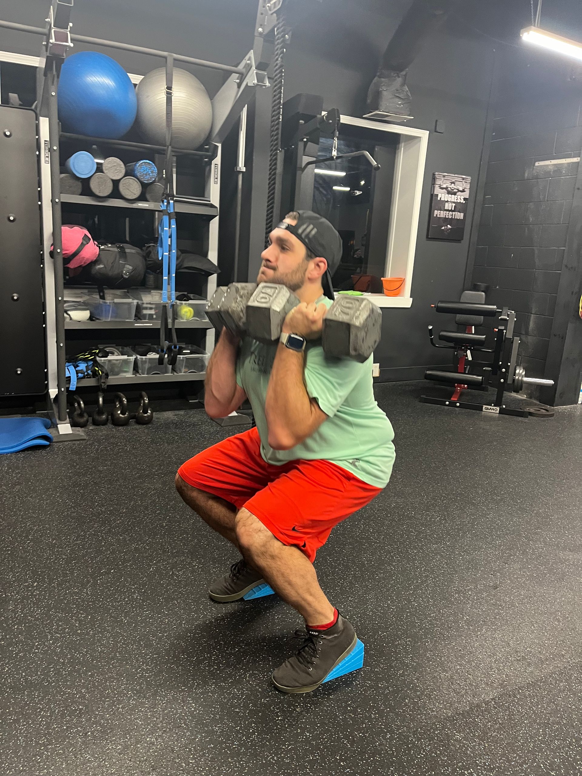 A man is squatting with a dumbbell on his shoulders in a gym.