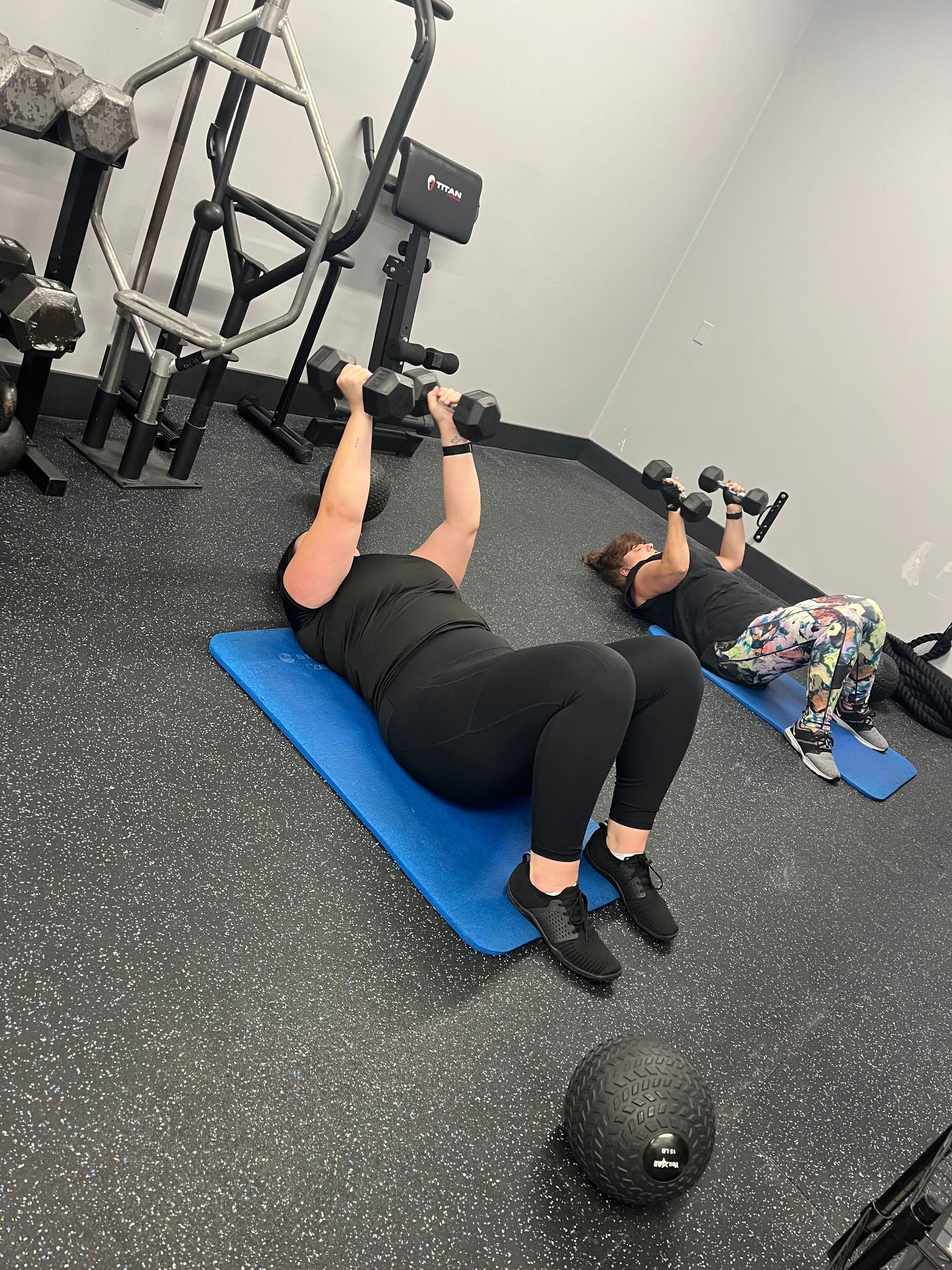Two women are doing exercises with dumbbells in a gym.