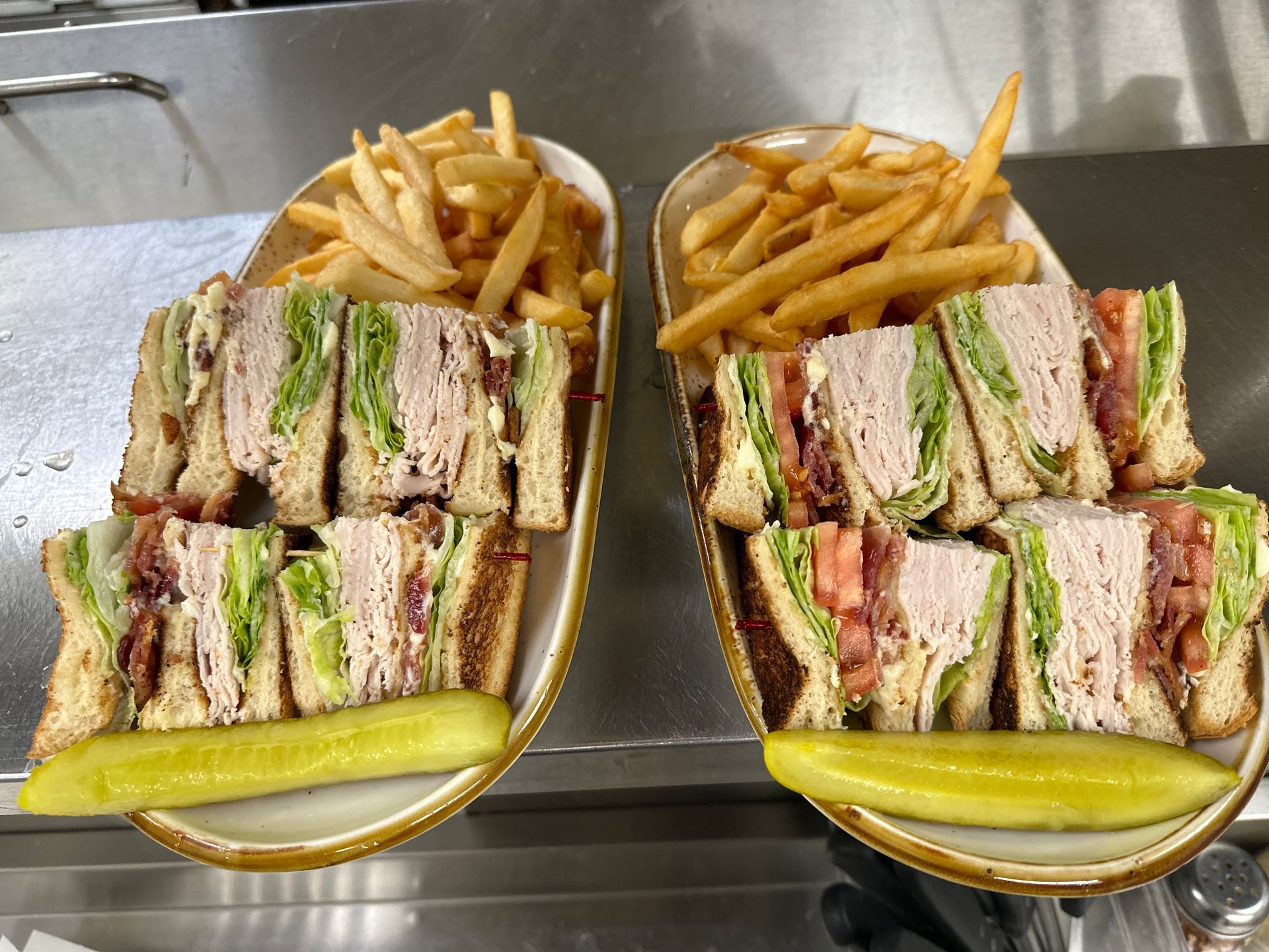 Two meatball subs with french fries and pickles on a tray on a shelf.