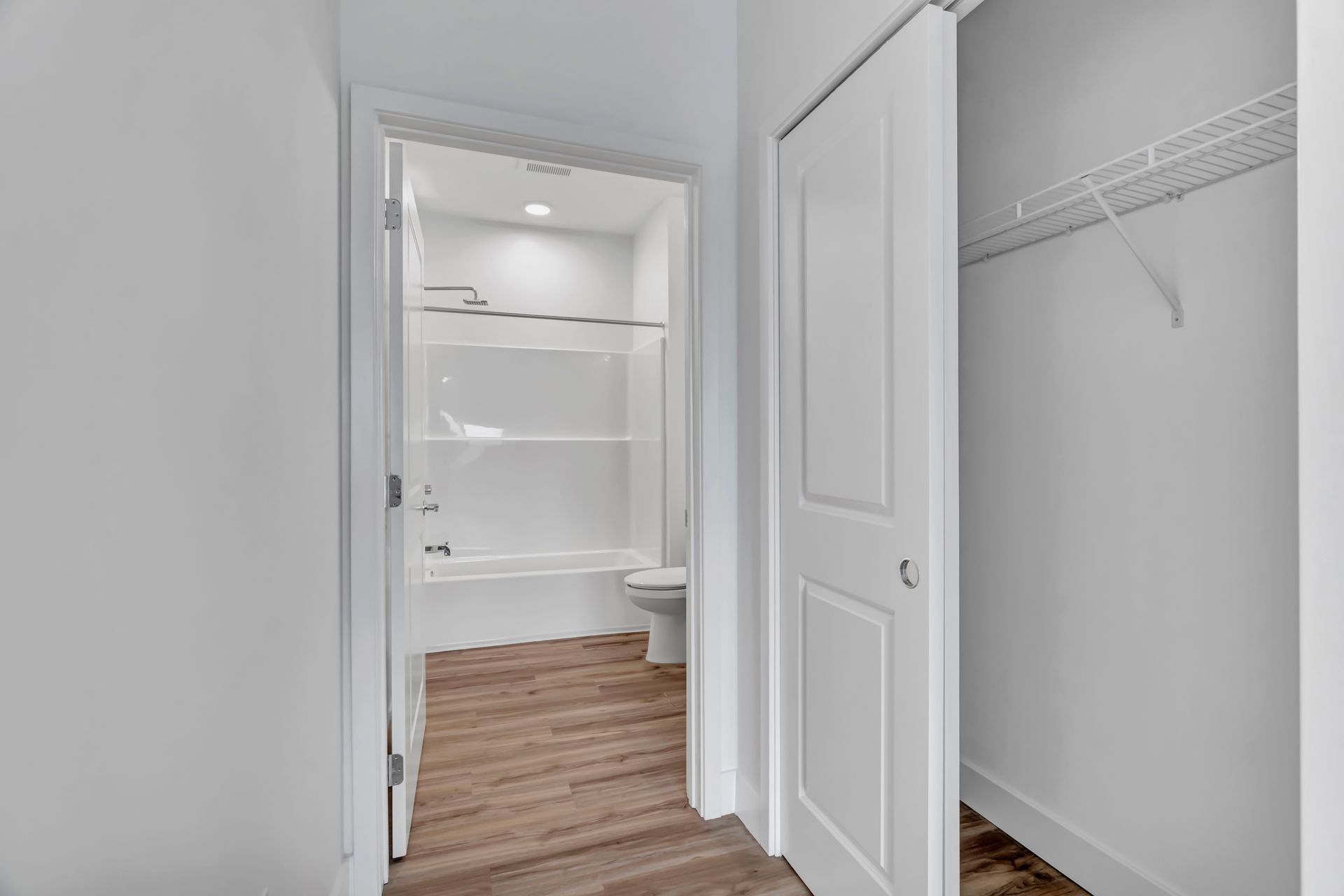Hallway with open bathroom and closet doors. White walls, wood-look floor.