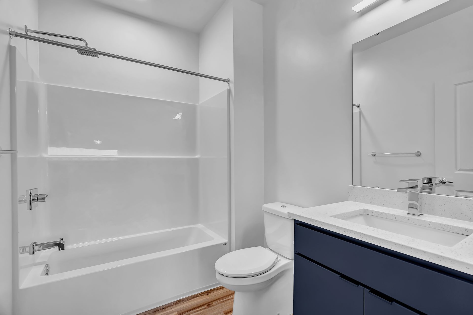 Bathroom with white tub/shower, blue vanity, and white toilet.
