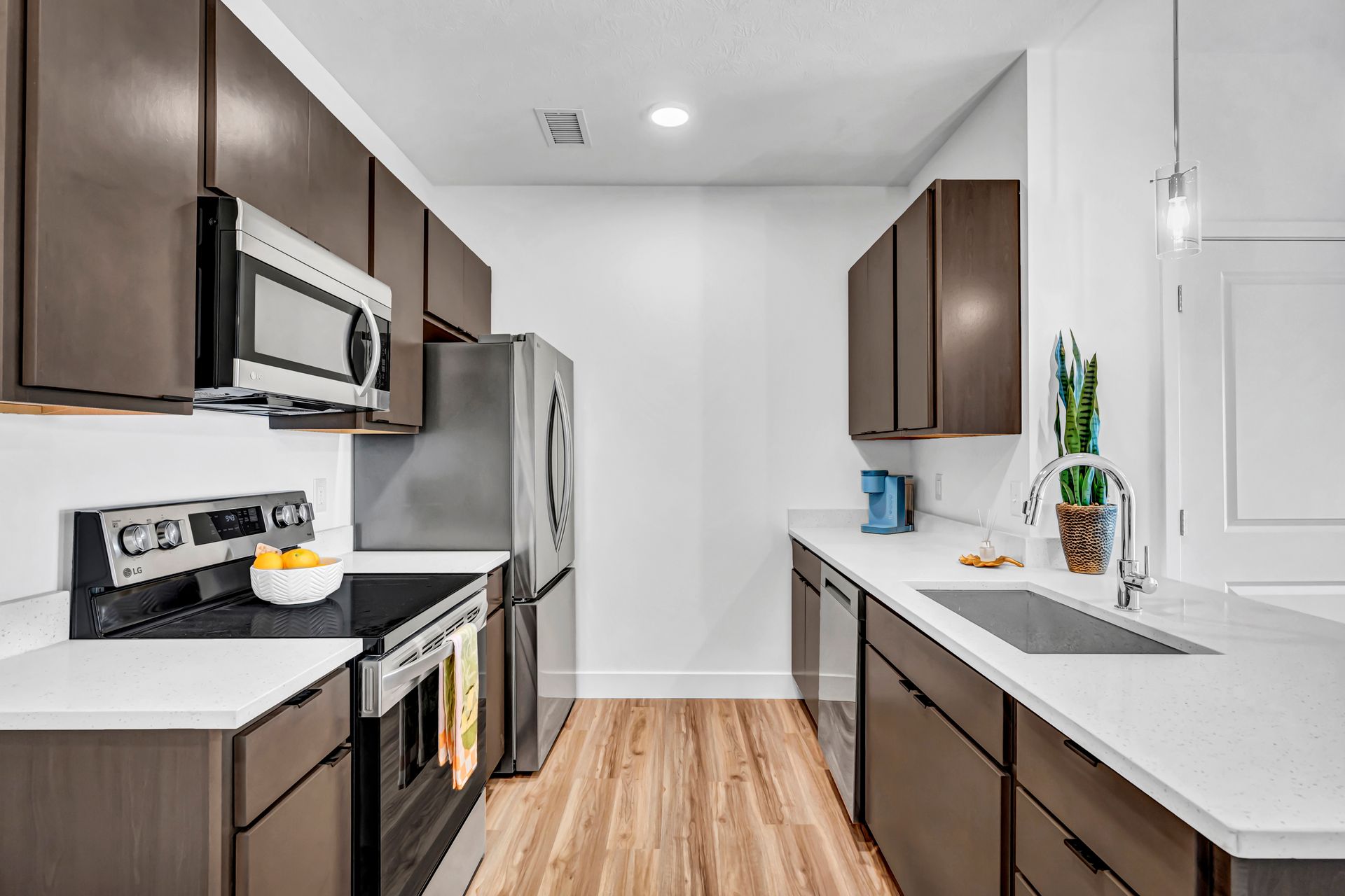Modern kitchen with dark brown cabinets, stainless steel appliances, and white countertops.