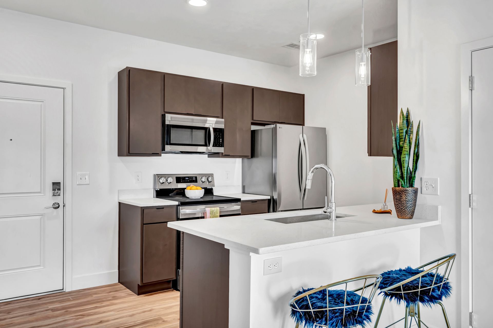Modern kitchen with brown cabinets, stainless steel appliances, white countertops, and bar stools.
