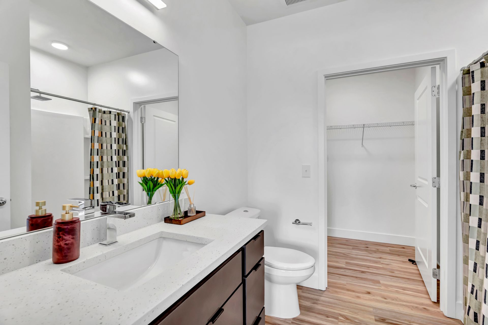 Modern bathroom with white walls, large mirror, and brown vanity. Open doorway to closet.