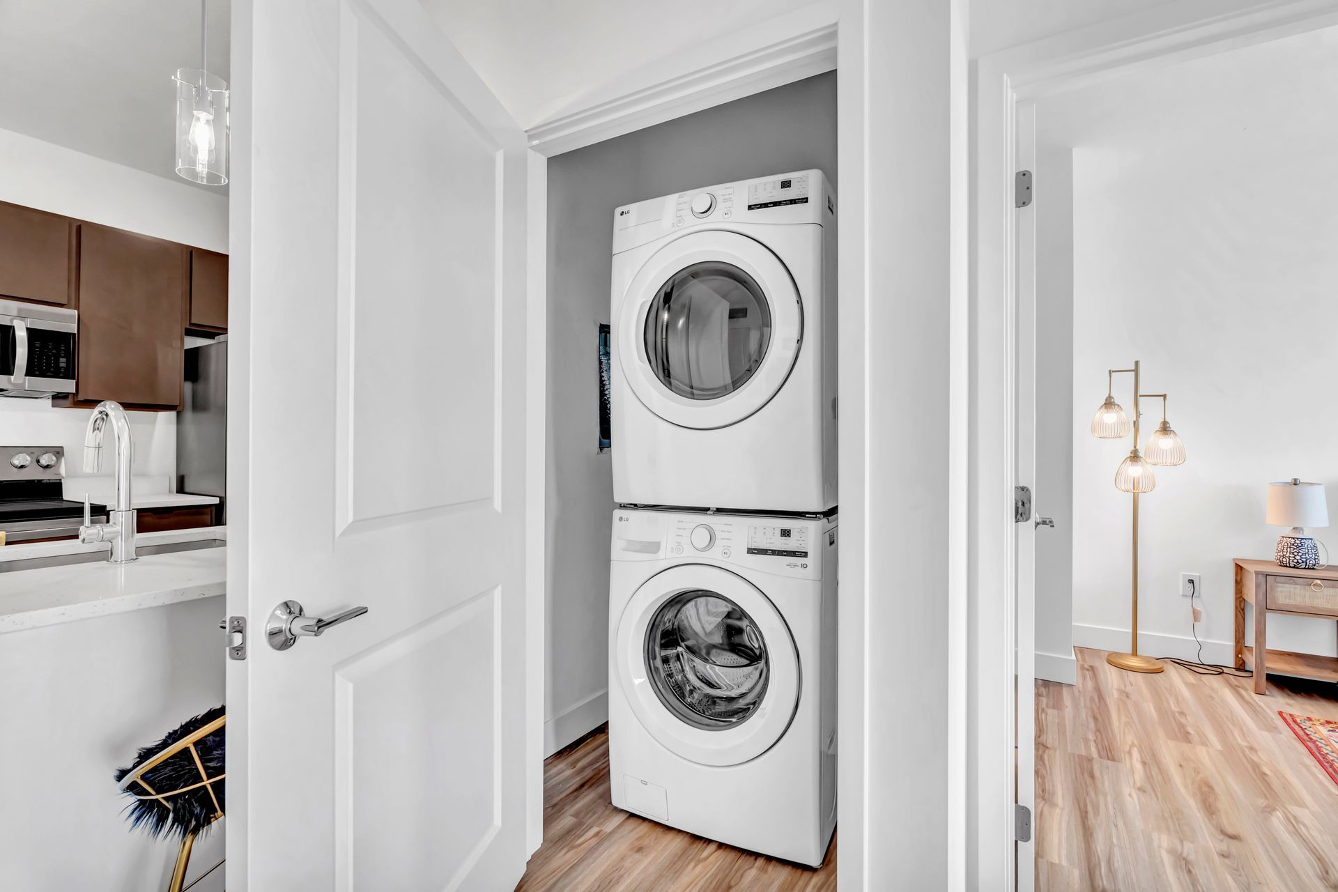 A stacked washer and dryer unit inside a closet, next to a kitchen and living area.