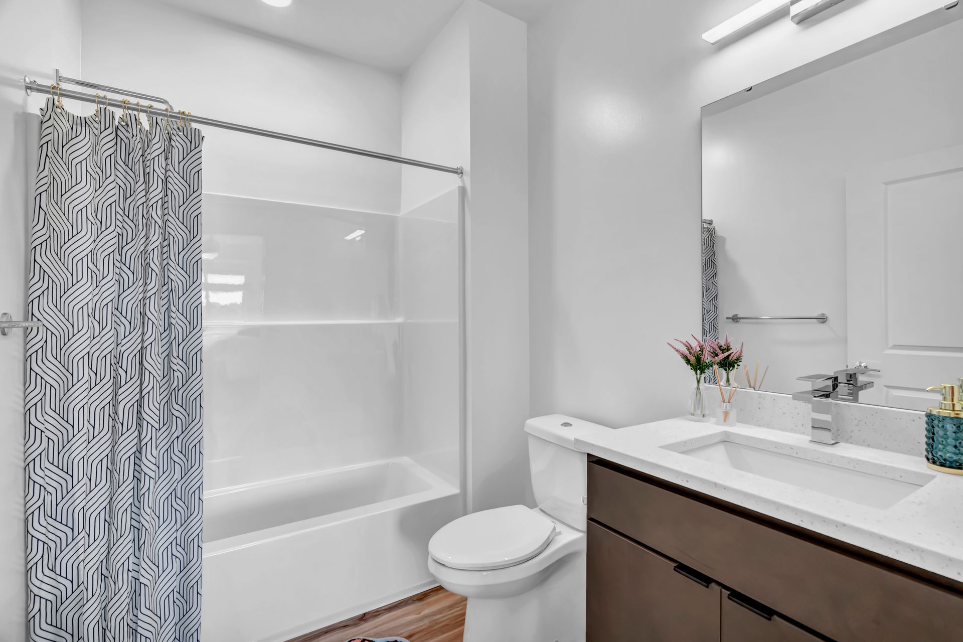 Bathroom with white tub, toilet, and vanity. Geometric patterned shower curtain.