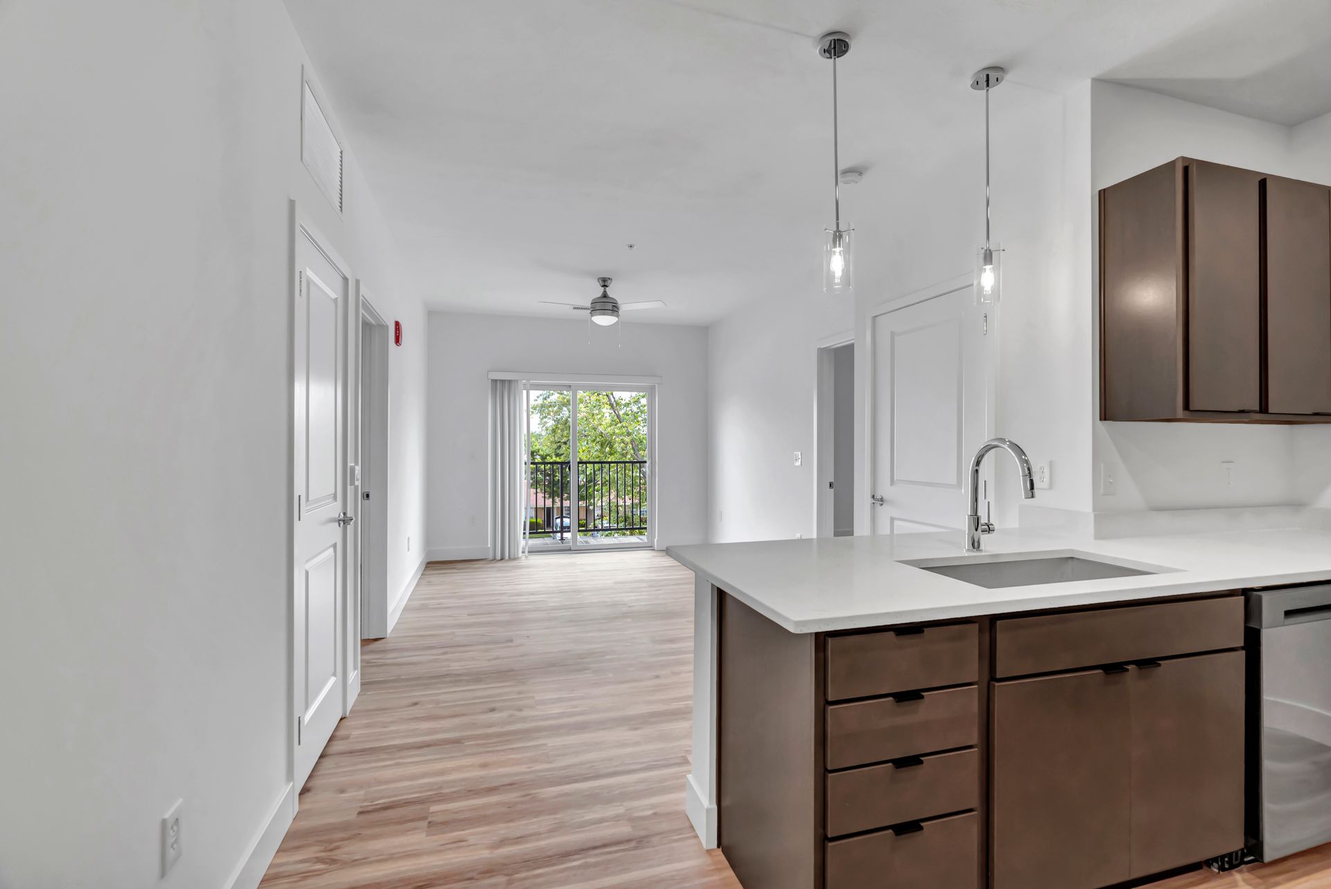 Interior view of a modern kitchen with an island, hardwood floors, and sliding glass door to a balcony.