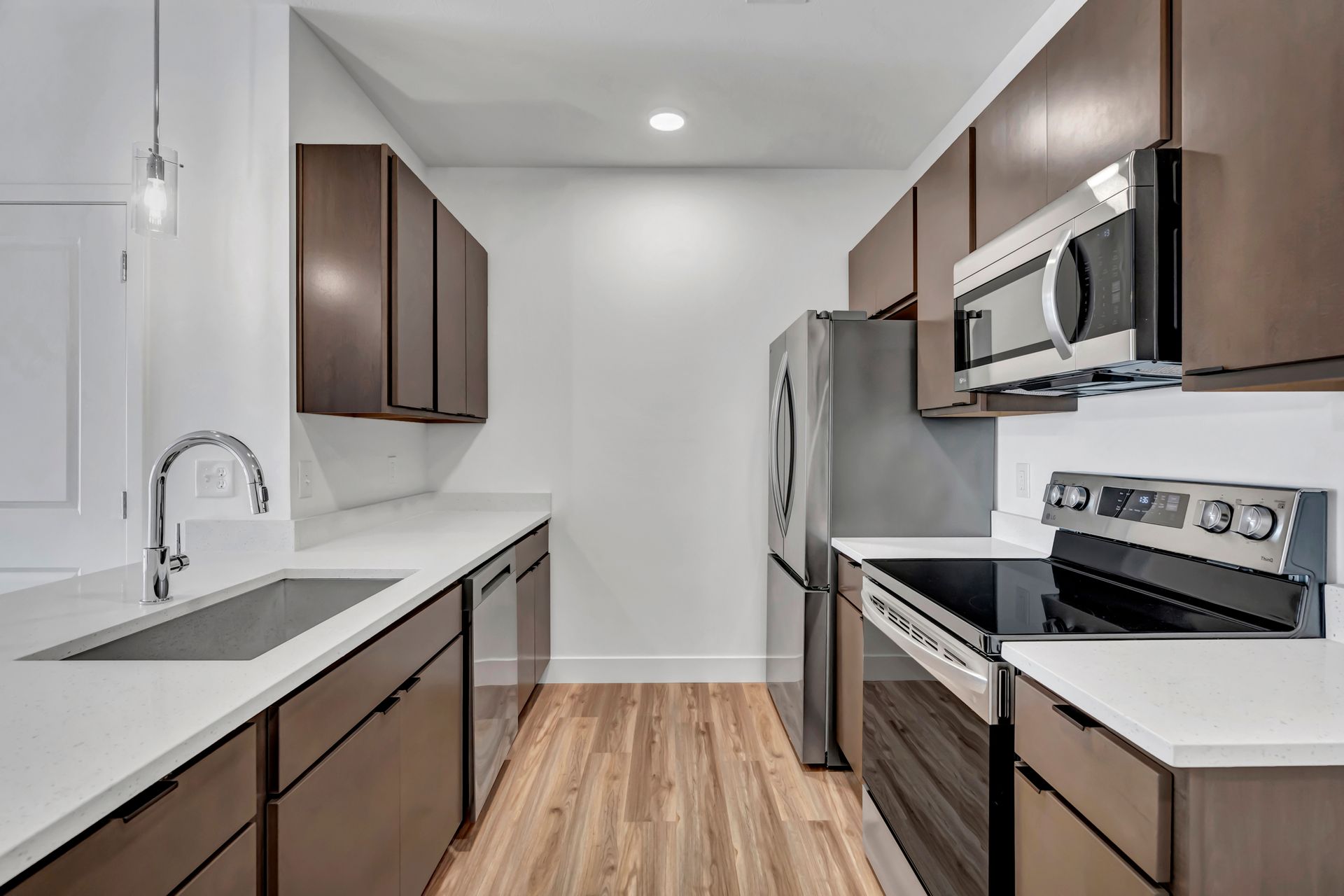 Modern kitchen with dark wood cabinets, stainless steel appliances, and white countertops.