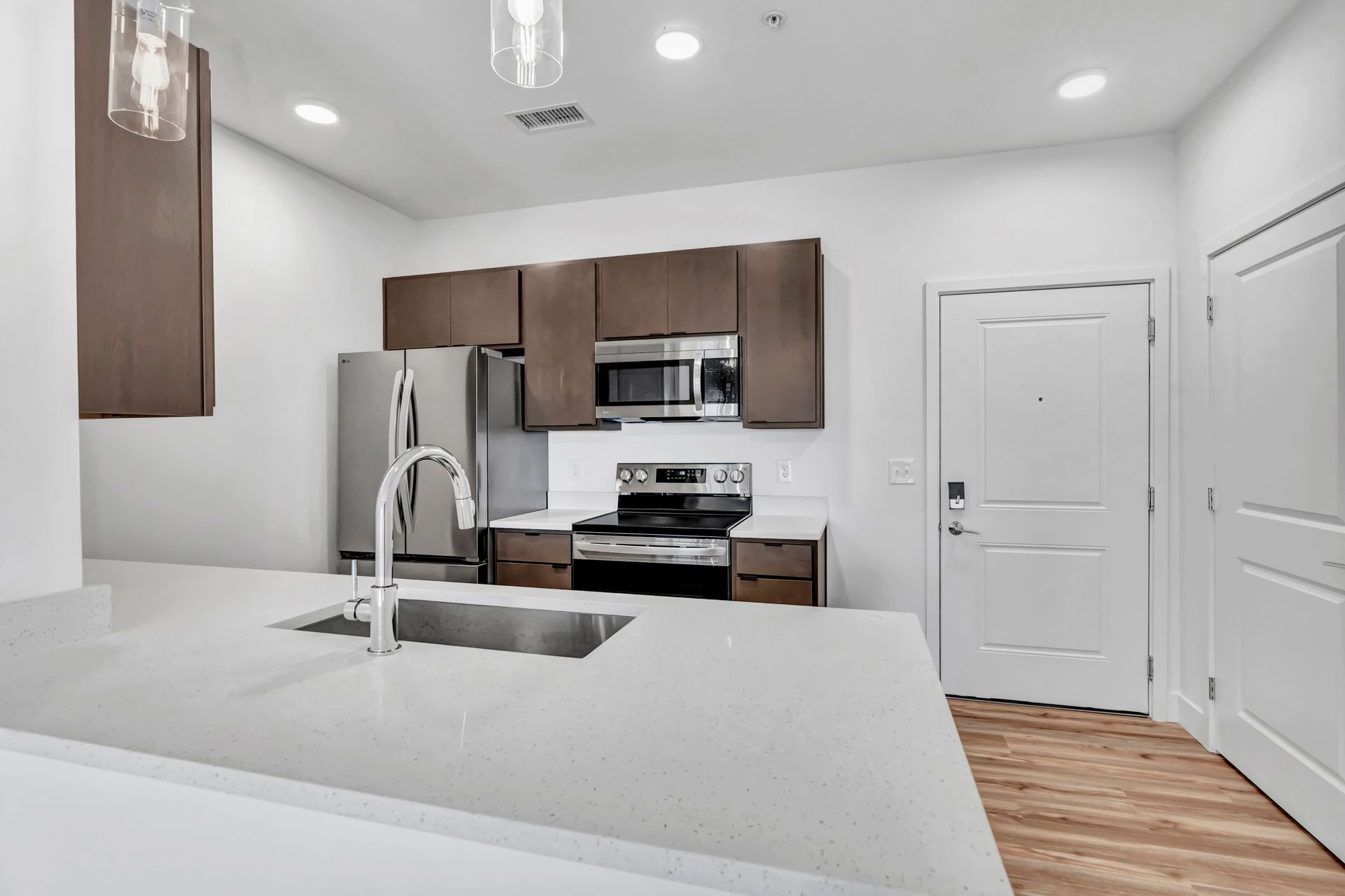 Modern kitchen with stainless steel appliances, light countertops, and dark brown cabinets.