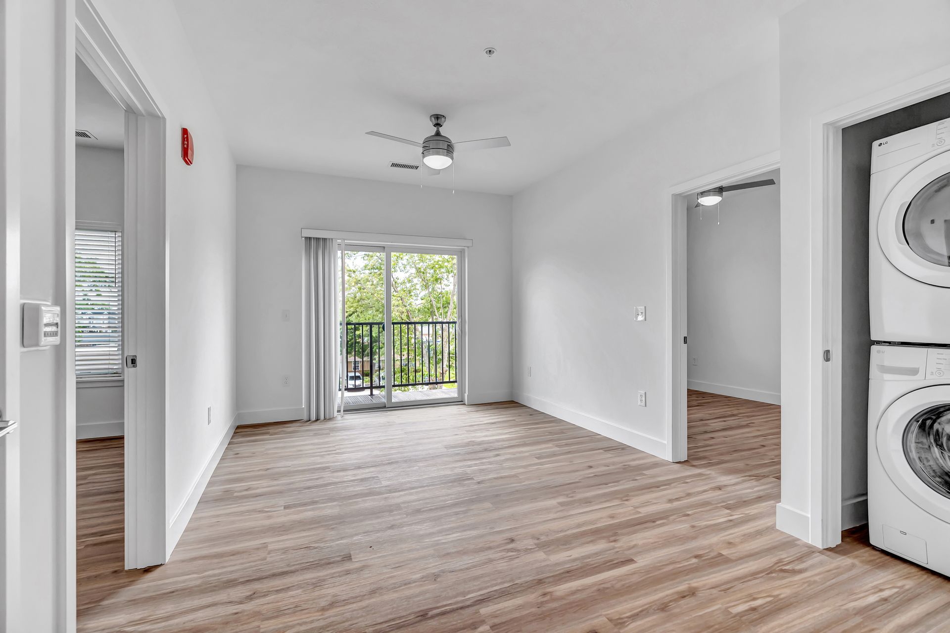 Bright white apartment interior with balcony and stacked washer/dryer; light brown carpet and wood flooring.