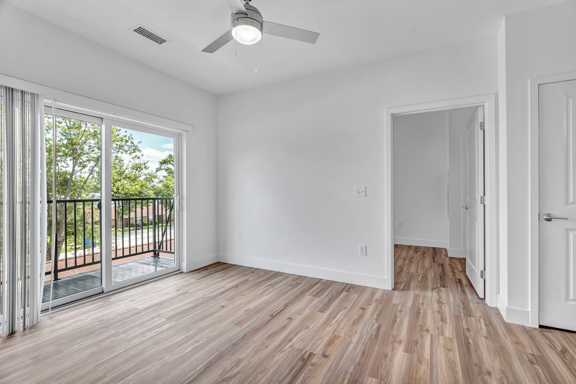 Bright, empty room with wood floors, balcony access, and white walls.