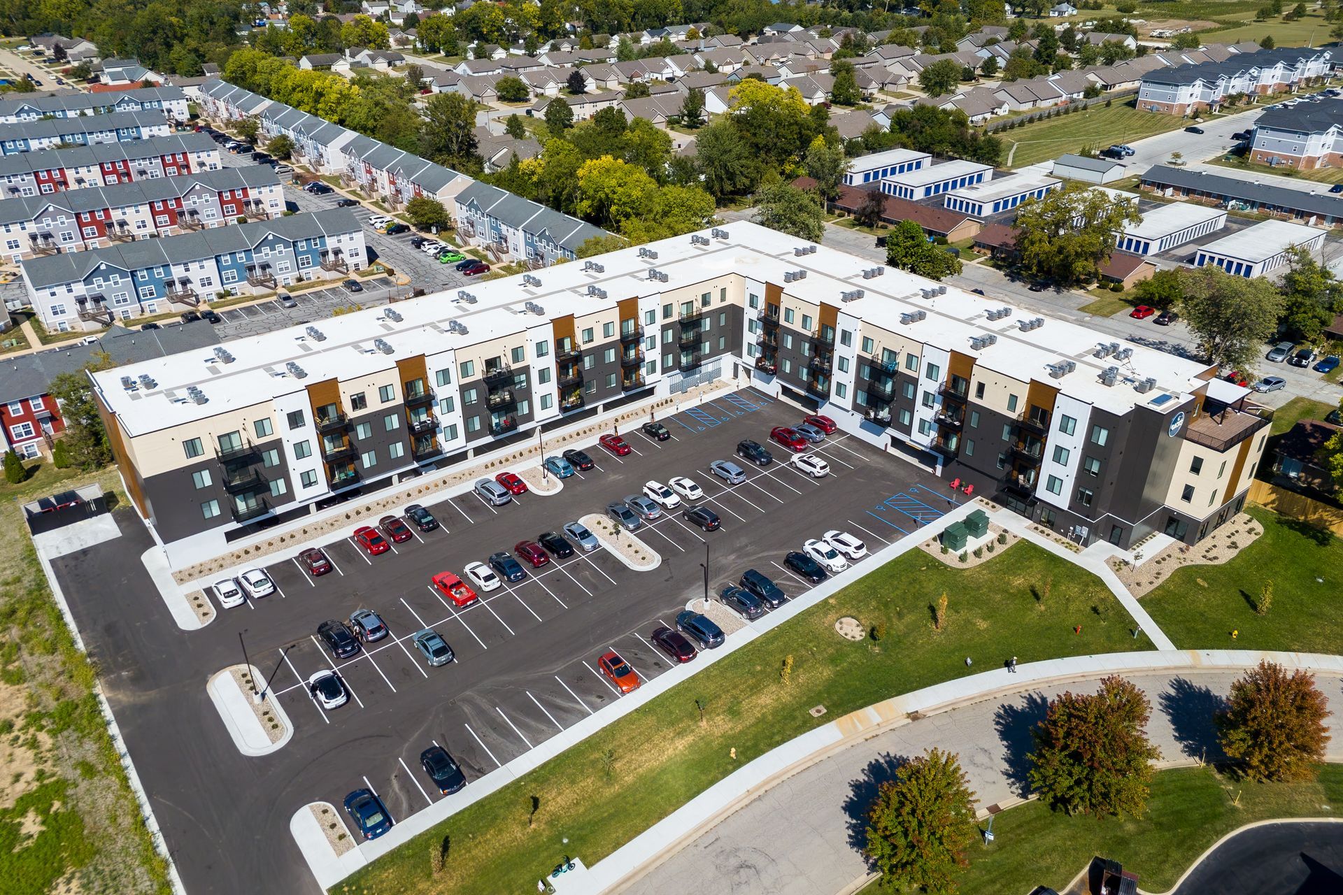Aerial view of a multi-story apartment building with a large parking lot and surrounding residential area.