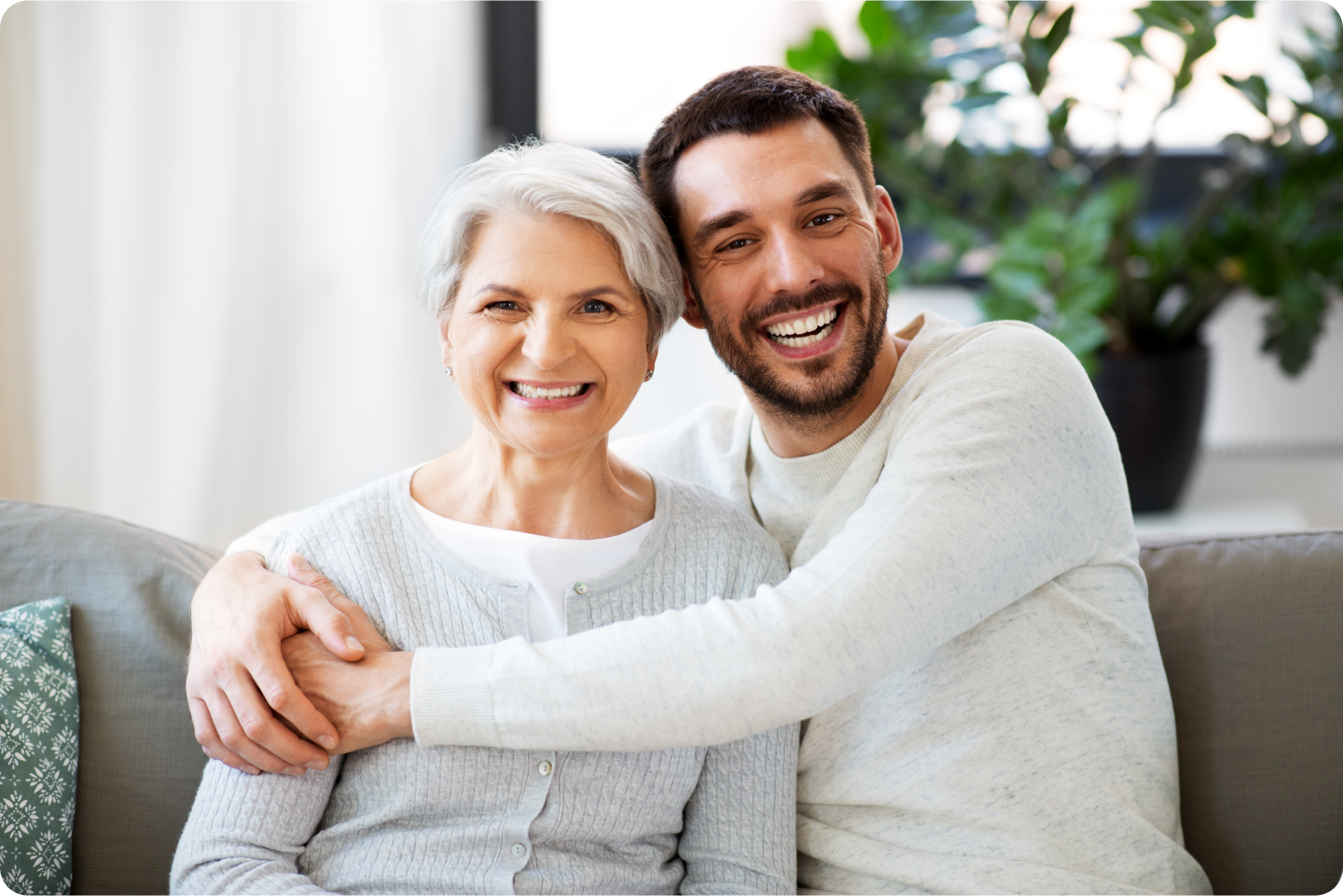 A man is hugging an older woman while sitting on a couch.