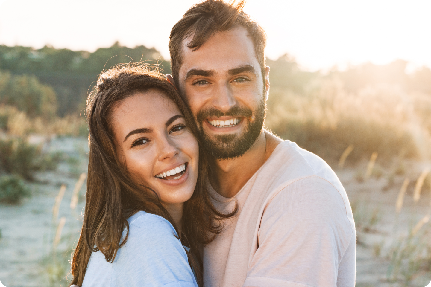 A man and a woman are hugging each other and smiling for the camera.