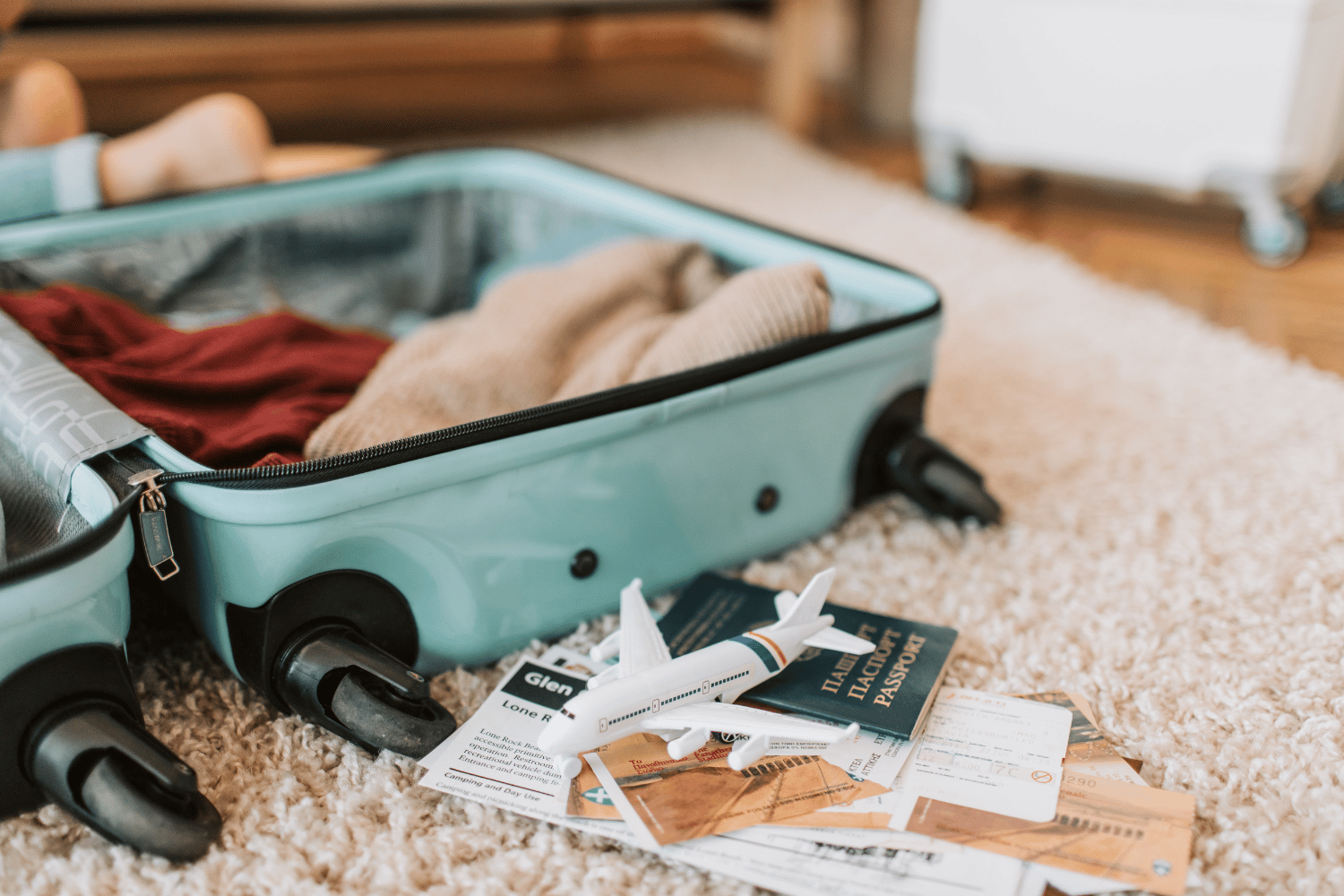 Open suitcase on floor with folded clothes, travel documents, and shoes scattered beside it