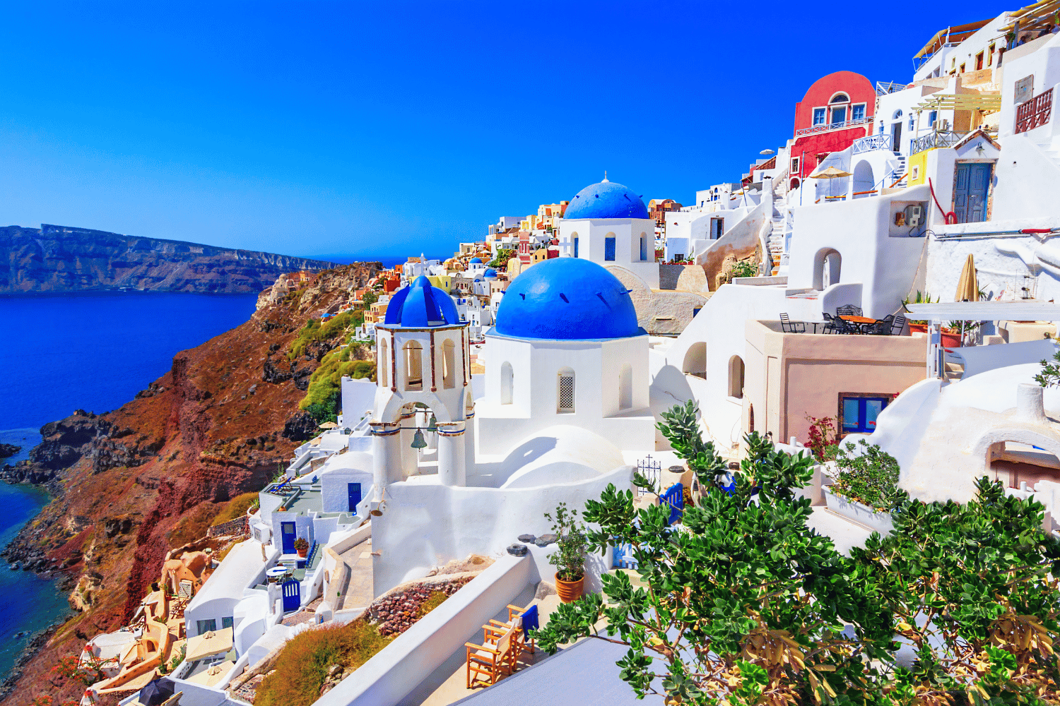 Whitewashed buildings with blue domes on a cliffside overlooking the Aegean Sea in Santorini, Greece.